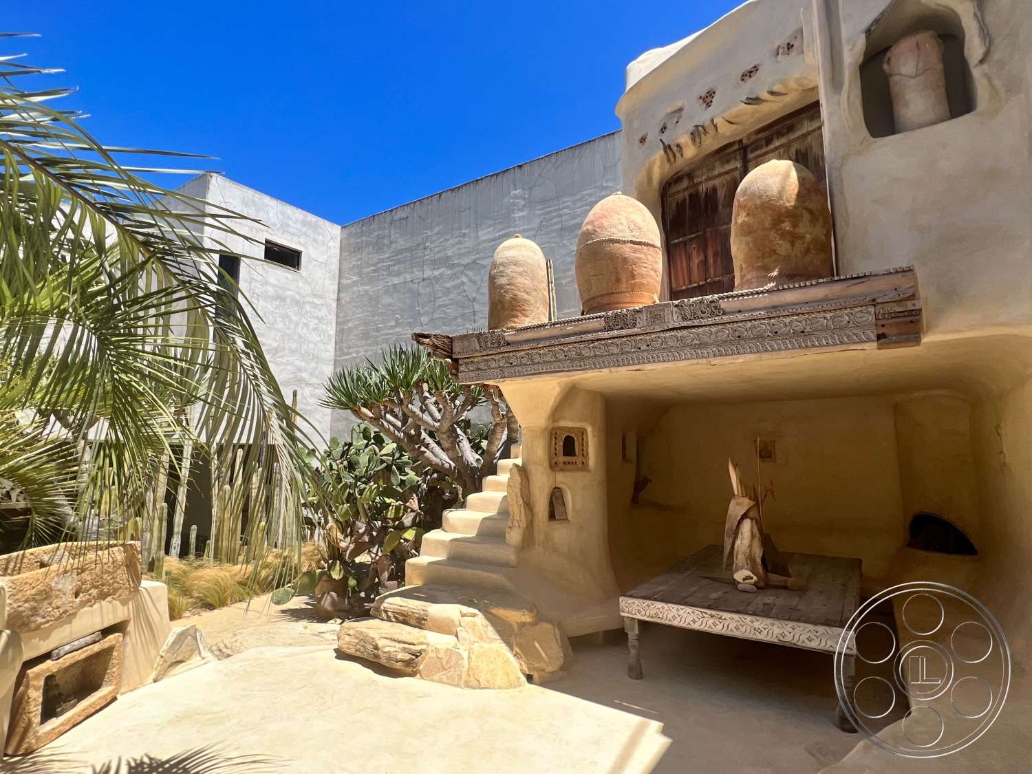 Hand-plastered courtyard with rounded stairs, carved wood trim, wall niches and oversized clay urns on a ledge at the Oasis filming location in Venice