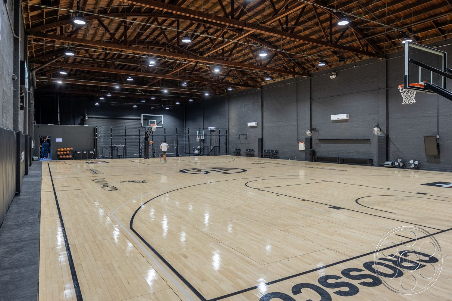 Full hardwood basketball court under a high timber-truss roof with dark painted brick walls at Gym 36, a warehouse basketball gym filming location in Downtown Los Angeles