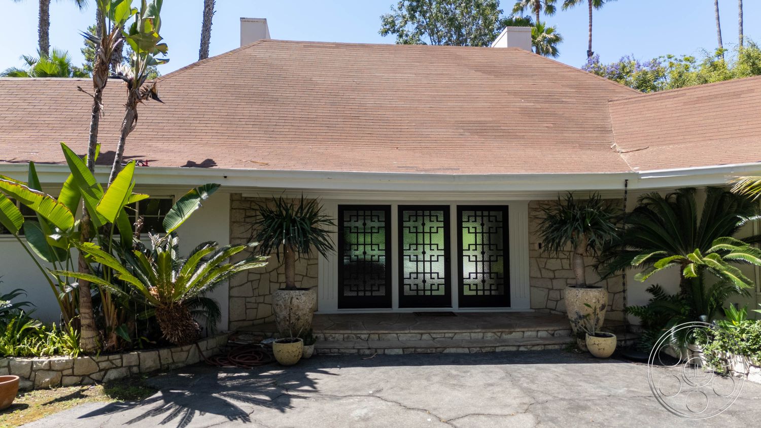 MCM 23 - minimalist decor, natural light, exterior, Mid-Century Modern, outdoor space, palm trees, earthy tones, greenery, concrete pathway, sloped roof, decorative planters, unique design elements, urban oasis, tropical landscaping, garden area, architectural detail, stone facade, front entrance, spacious front yard, black glass doors, entrance steps