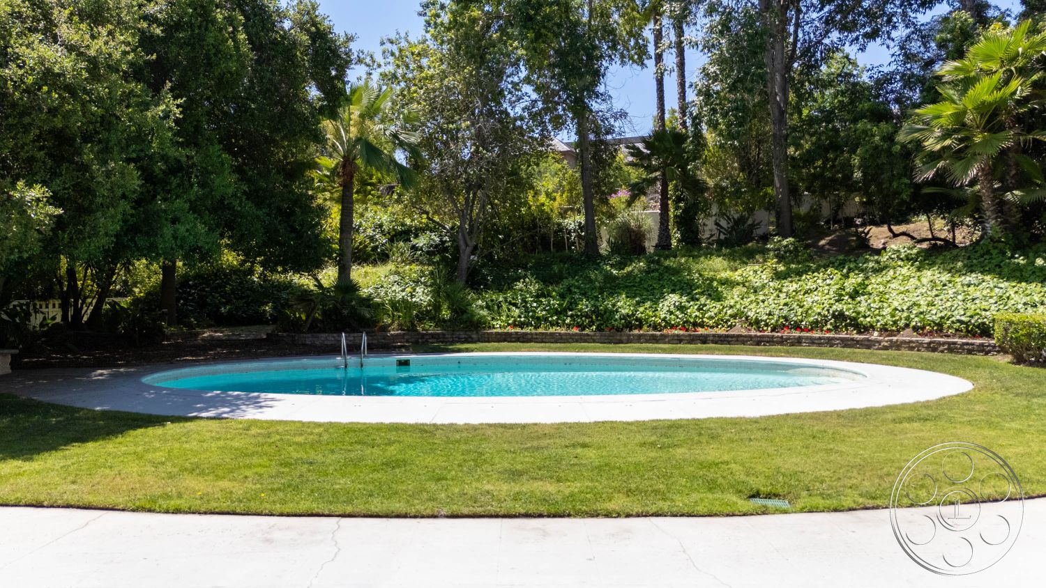 MCM 23 - natural light, exterior, landscaped garden, lush greenery, palm trees, tropical plants, concrete patio, private backyard, swimming pool, green lawn, family-friendly setting, relaxing environment, modern outdoor space, garden beds, oval pool, healthy foliage, curved pool edges