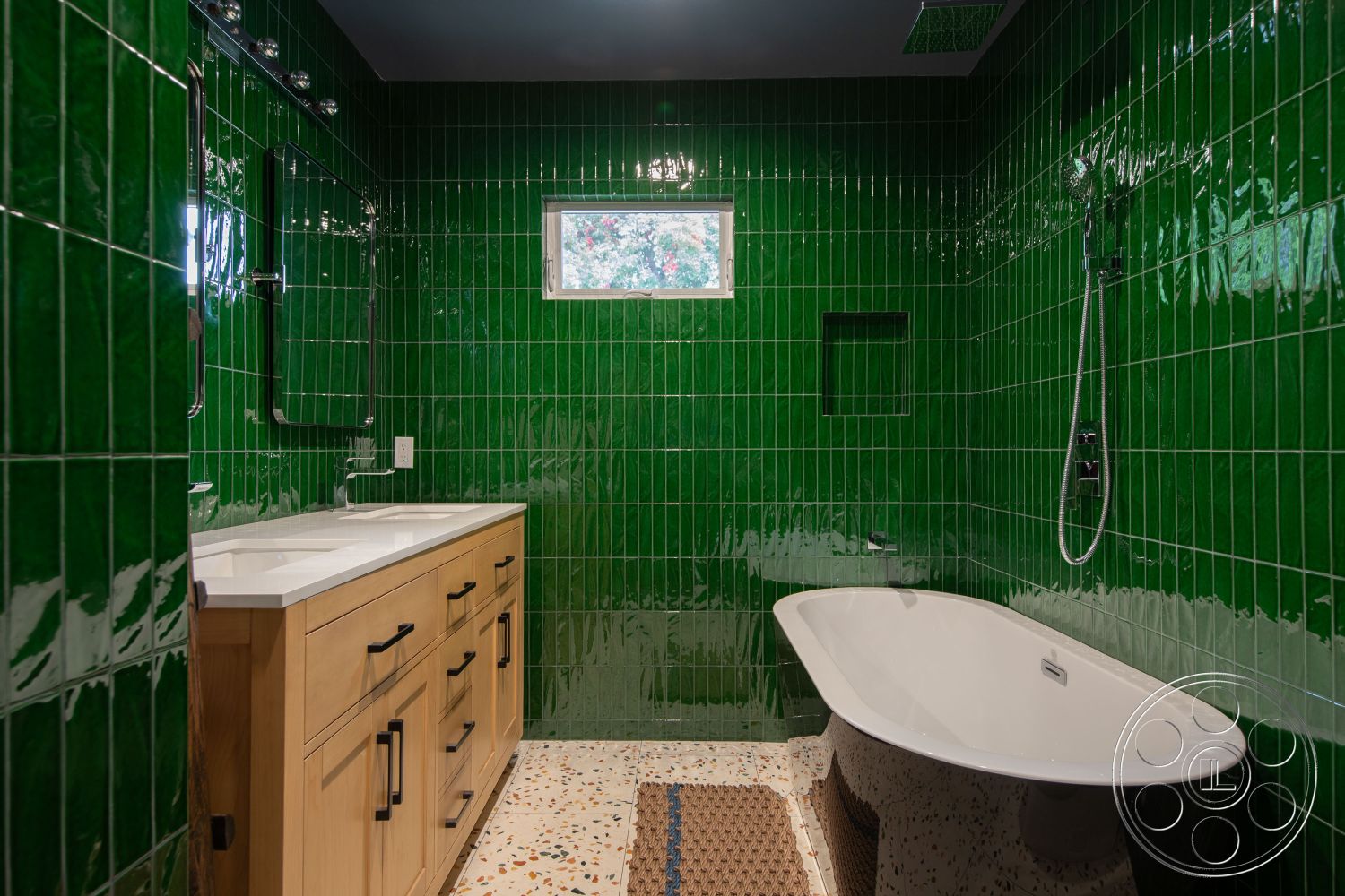 Bungalow 56 - interior bathroom design, green glossy tile bathroom walls, white quartz countertop vanity, wooden bathroom cabinet with black handles, freestanding oval bathtub, textured beige bath mat flooring, shower with modern chrome fixtures, rectangular window providing natural light, exposed shower plumbing, smooth pebble mosaic floor, modern bathroom space