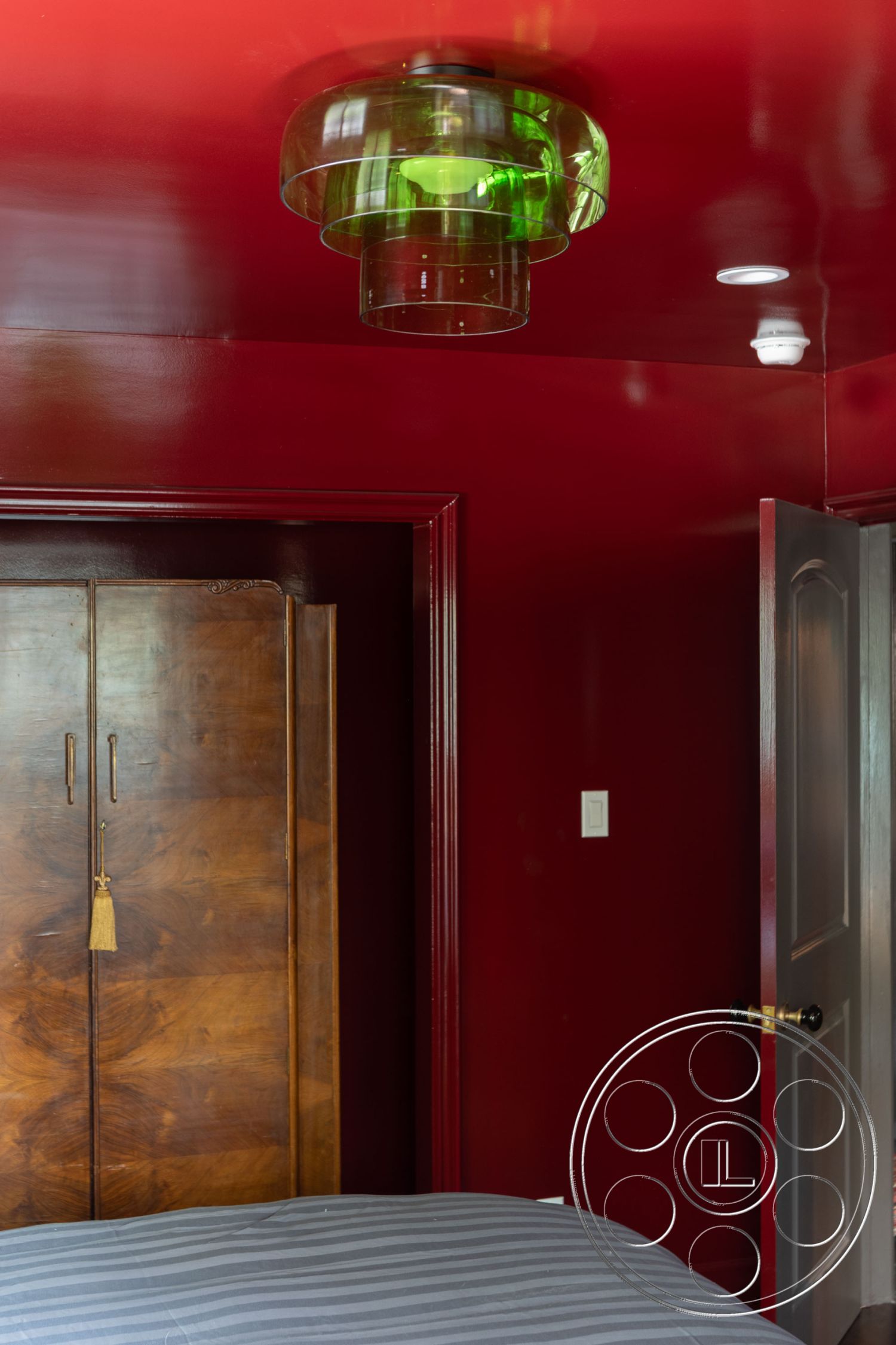 Bungalow 56 - modern pendant light fixture, cozy bedroom setting, burgundy painted walls, wooden wardrobe with brass handles, glass light shades, gray striped bedding, contemporary door with doorknob