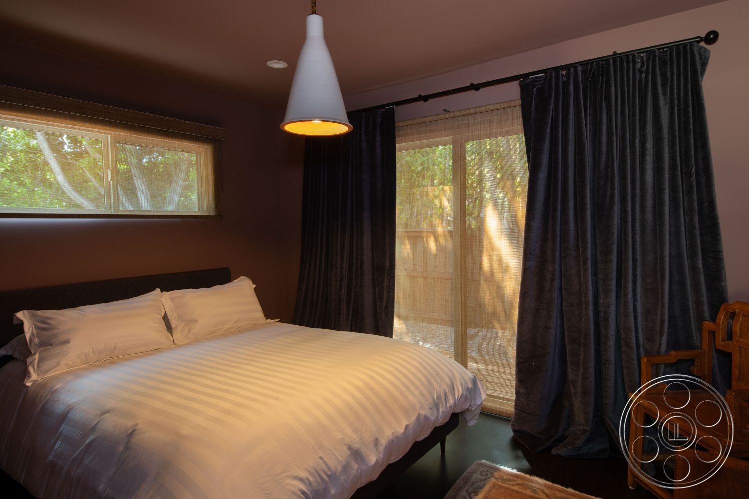 Bungalow 56 - natural light, contemporary decor, floor-to-ceiling windows, neutral wall color, wooden accent chair, modern rustic style, sheer window treatments, dark hardwood bedroom floors, interior bedroom design, plush white bedding, striped duvet cover, textured dark curtains, minimalist pendant lighting, cozy bedroom atmosphere