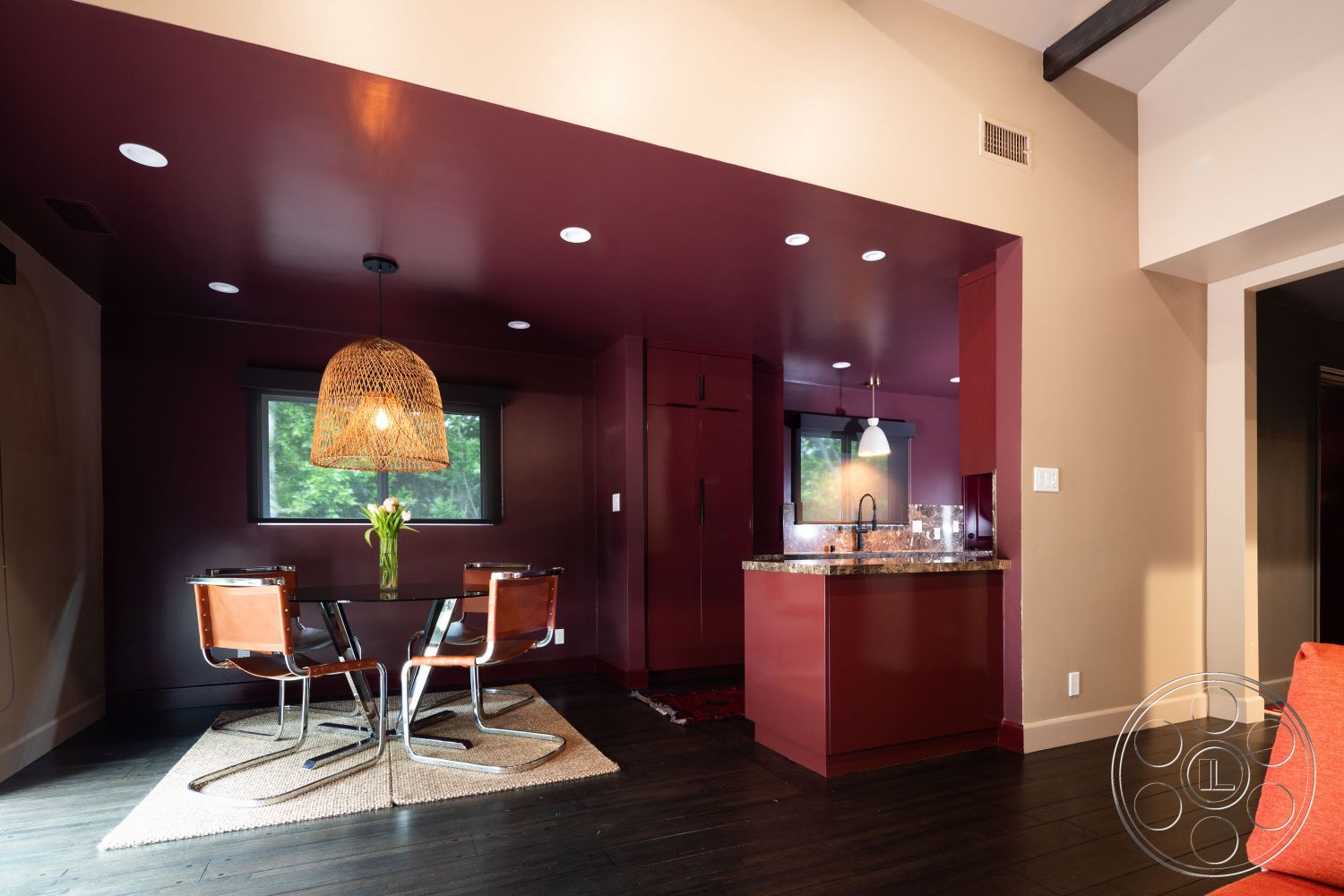 Bungalow 56 - minimalist aesthetic, textured area rug, open concept layout, modern pendant lighting, floor-to-ceiling windows, neutral wall color, granite countertop, round dining table, sustainable design, mid-century modern style, recessed ceiling lights, woven pendant lamp, walnut hardwood flooring, high-gloss burgundy kitchen cabinets, black metal dining chairs, corner window design