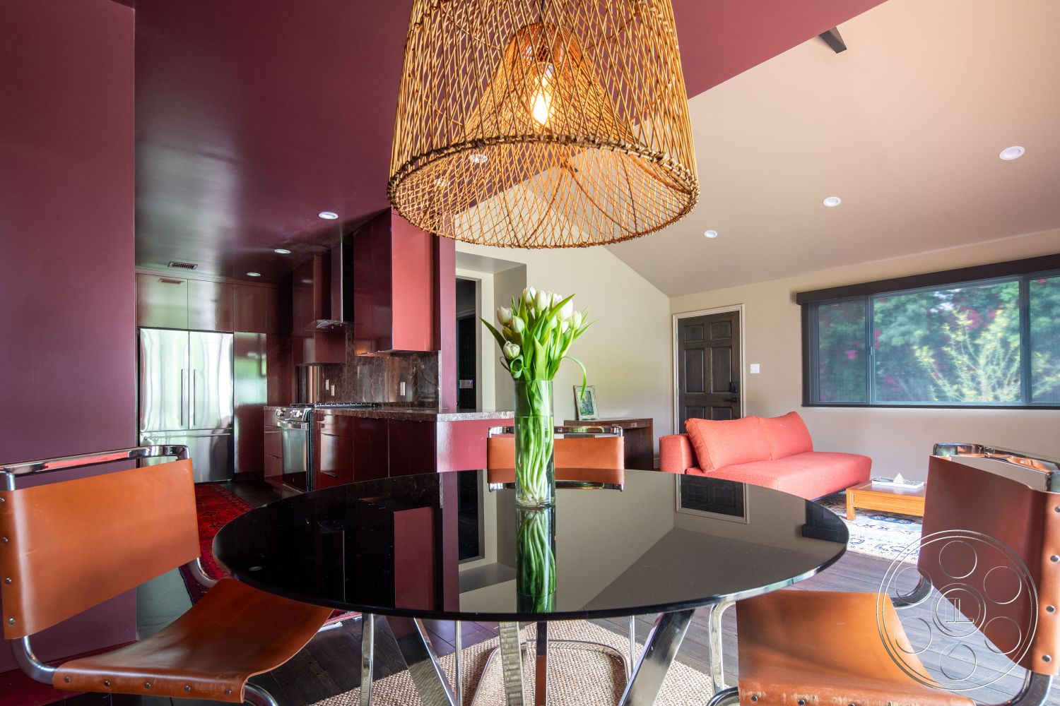 Bungalow 56 - hardwood flooring, decorative area rug, floor-to-ceiling windows, functional kitchen layout, black glass dining table, woven pendant light fixture, stainless steel kitchen appliances, leather dining chairs, interior modern dining area, dark wood kitchen cabinetry, stone kitchen countertops, plum painted accent wall, light-filled living room with large windows, contemporary sofa in warm red, open concept kitchen and dining space, minimalist interior design