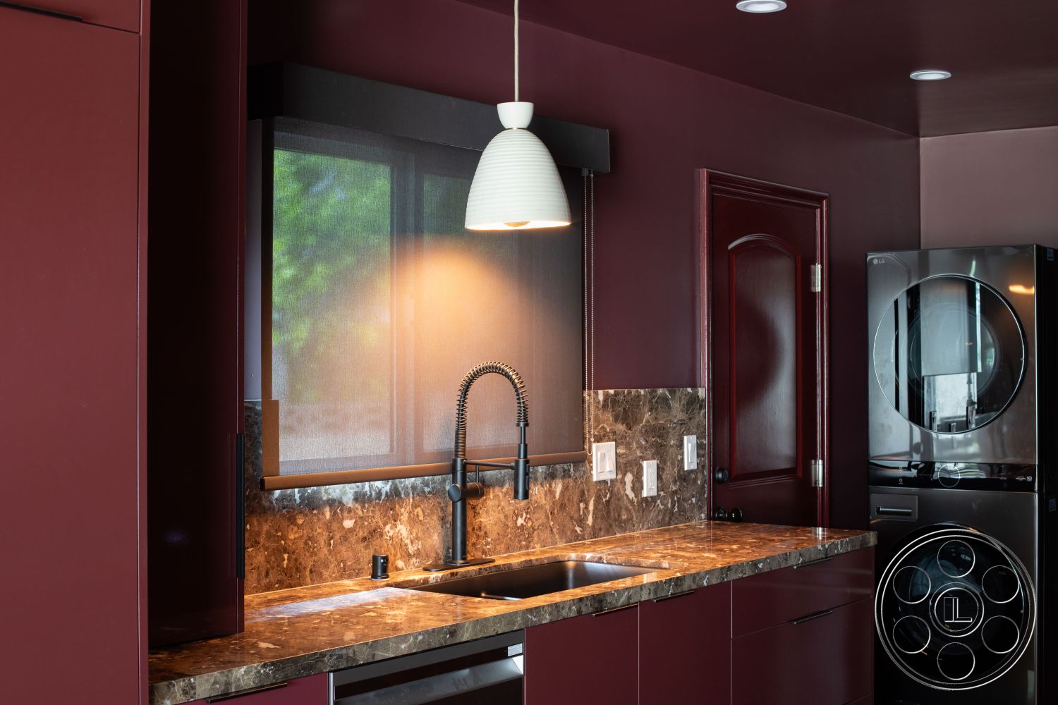 Bungalow 56 - dark wood cabinetry, recessed lighting, stainless steel appliances, modern pendant light fixture, interior kitchen space, modern minimalist design, high-gloss cabinet finish, black marble kitchen countertop, textured marble backsplash, sliding window with screen, washer and dryer area, white light switches, deep sink with pull-down faucet, burgundy wall paint, open layout kitchen, functional laundry area, contemporary wall treatment