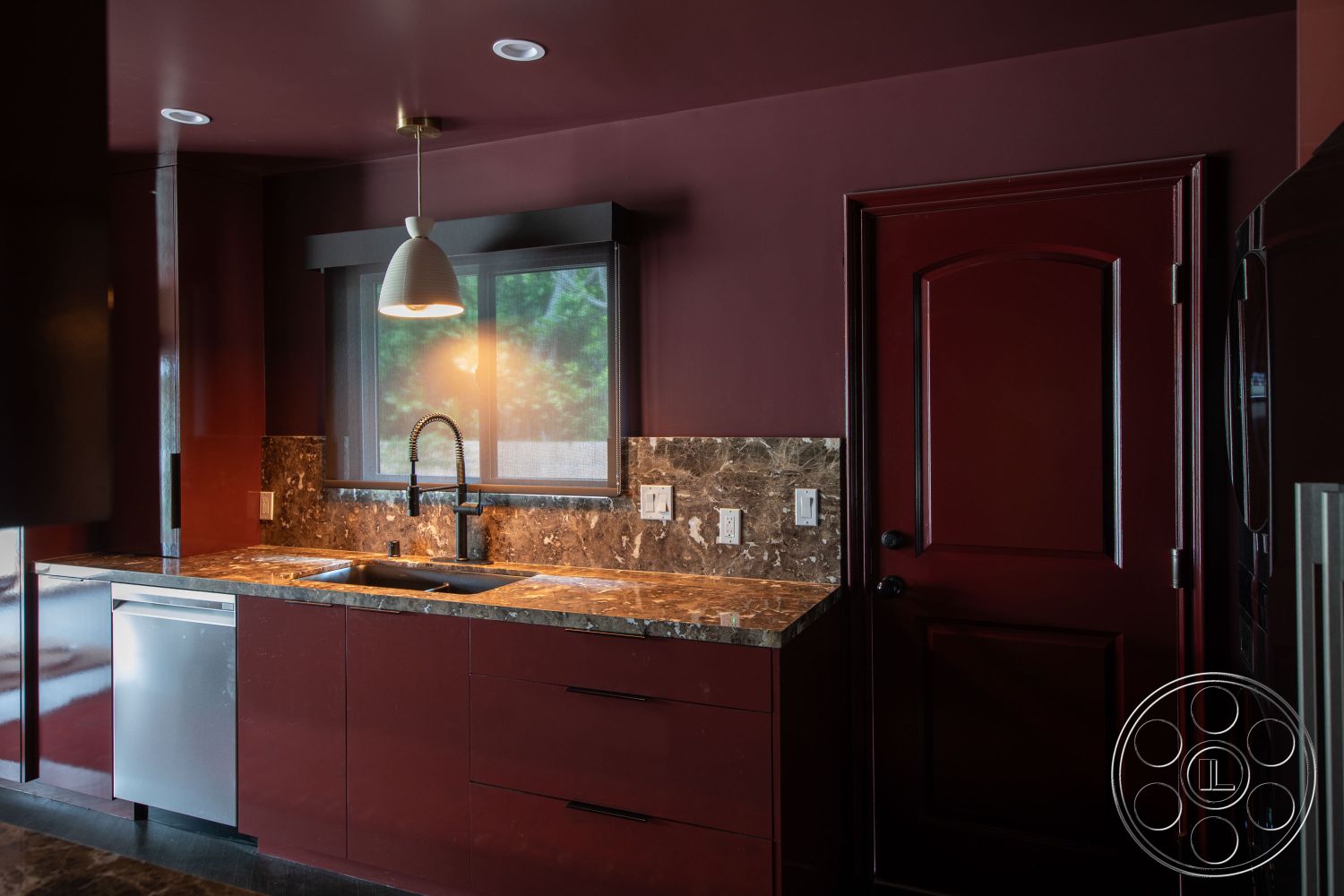 Bungalow 56 - dark wood cabinetry, marble countertop, decorative backsplash, modern faucet, interior kitchen, pendant lighting fixture, red painted walls, stainless steel dishwasher, black pull handles, large window with screen, dark floor tiles, solid wood door, undercabinet lighting