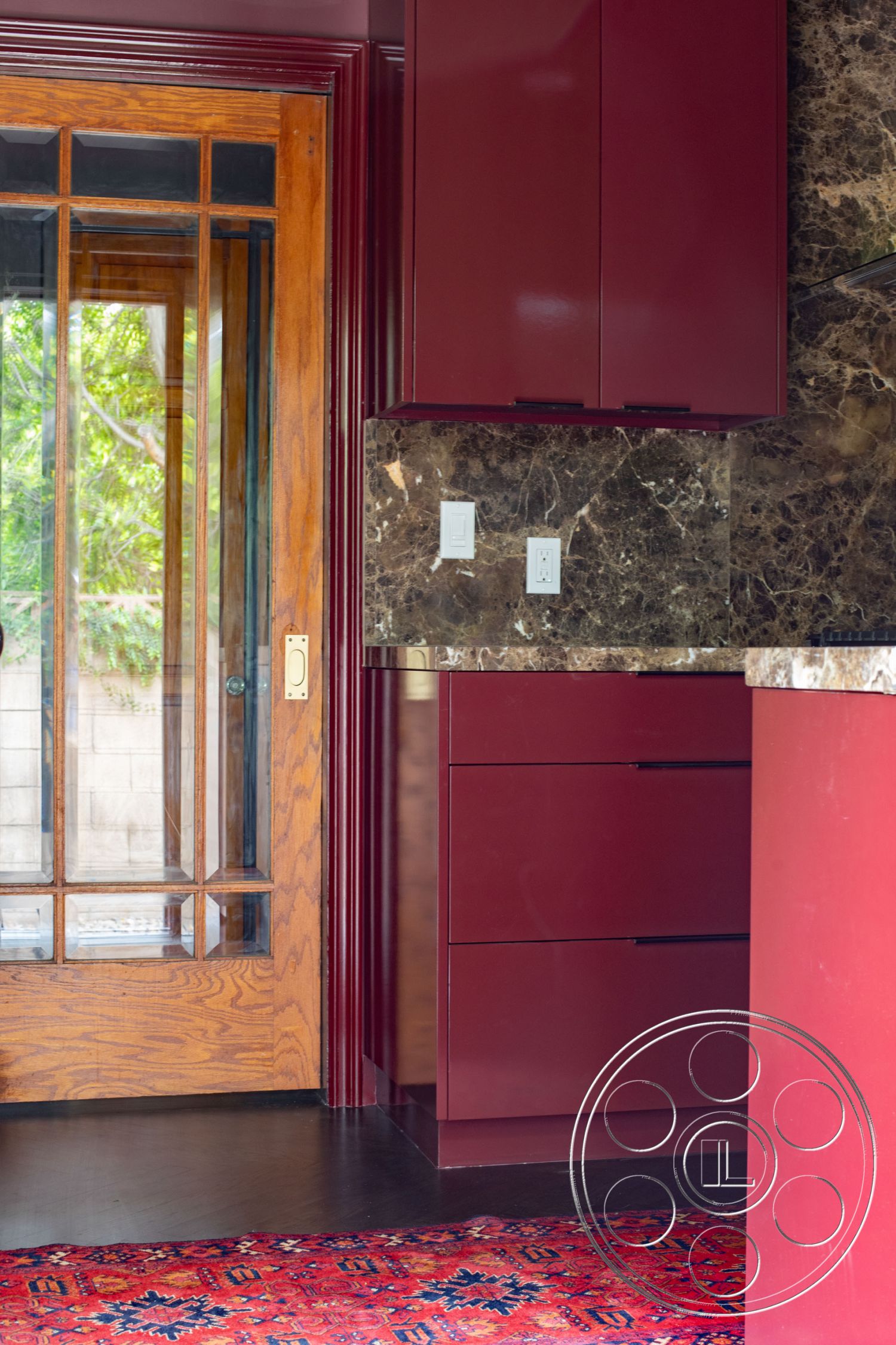 Bungalow 56 - custom cabinetry, high-end finishes, dark hardwood flooring, marble countertop, traditional rug, glass panel door, natural light from window, modern kitchen appliances, rich color palette, interior kitchen, burgundy cabinetry, dark wood entry door, exposed wood detailing, open-concept space