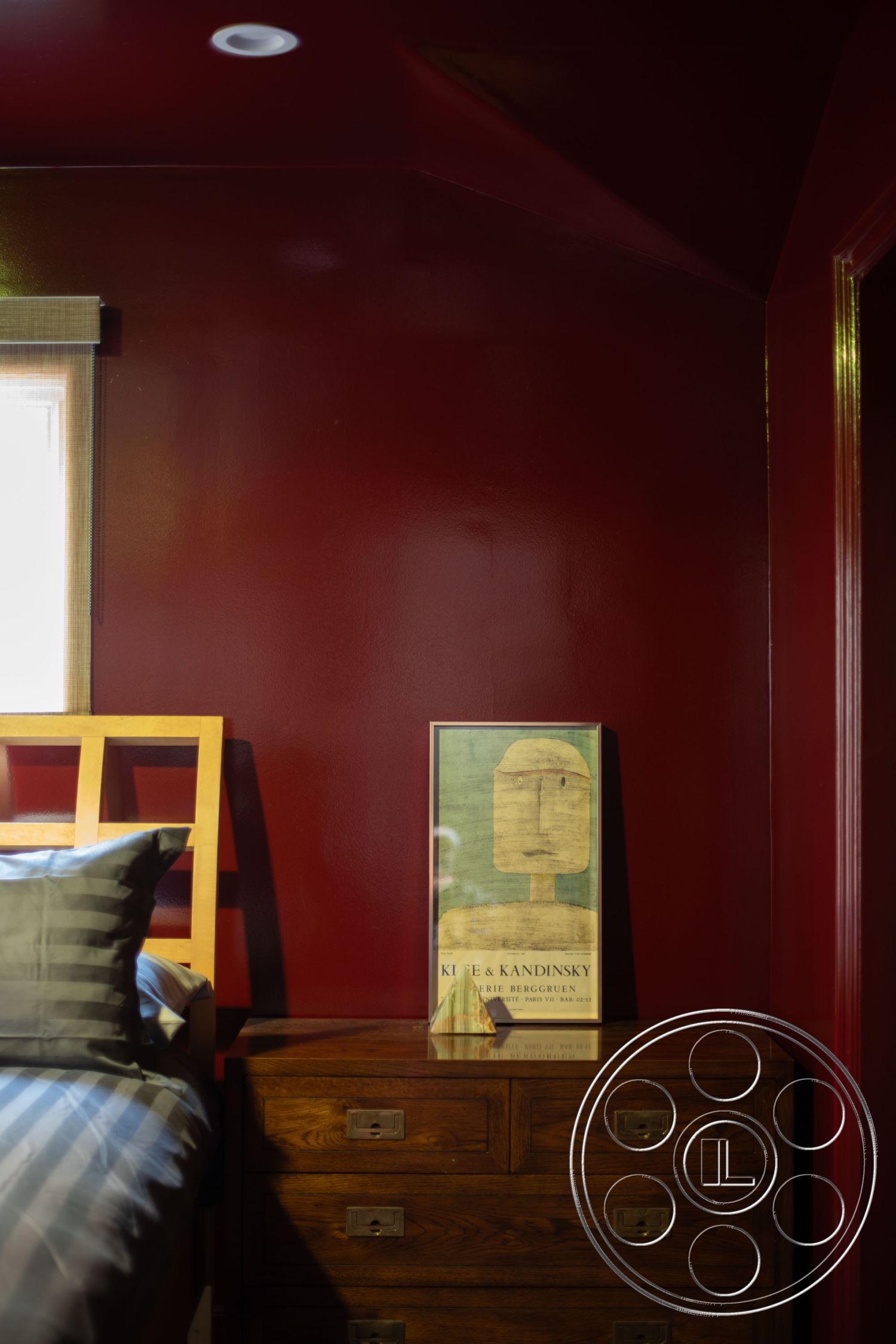 Bungalow 56 - modern decor elements, wooden nightstand, wooden bed frame, soft lighting fixtures, textured pillow, striped bedding, framed art print, dark red painted walls, minimalist room design