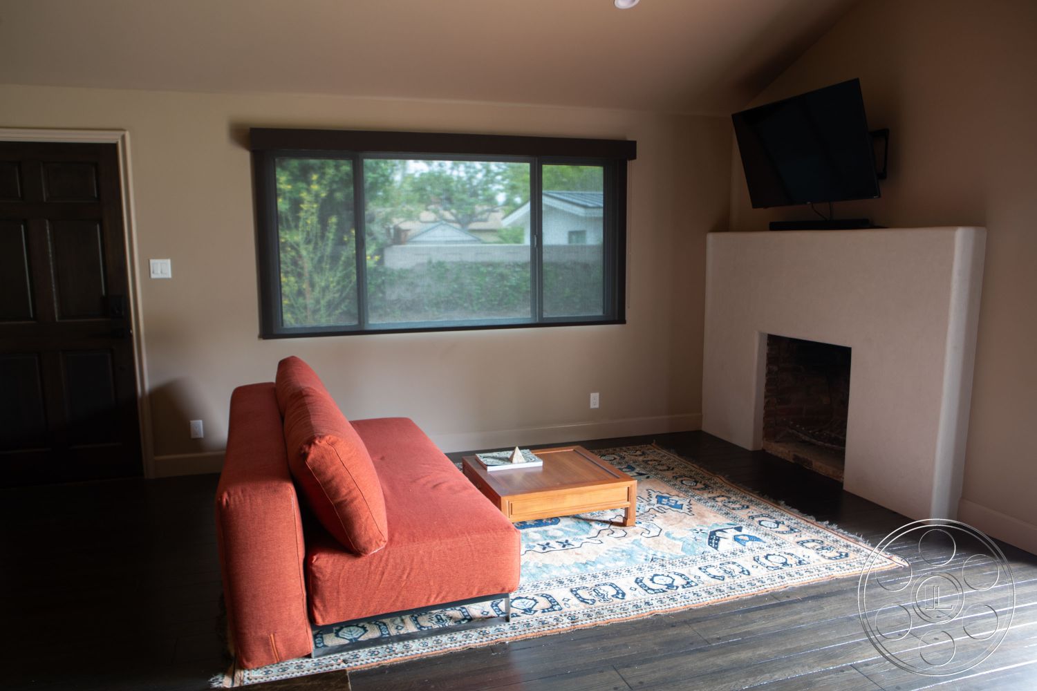 Bungalow 56 - textured area rug, casual seating area, hardwood floor, rectangular coffee table, natural light setting, interior living room, exposed brick fireplace surround, neutral painted walls, dark wood paneling accent wall, large rectangular windows, minimalist TV mounting, modern sofa design, open floor space