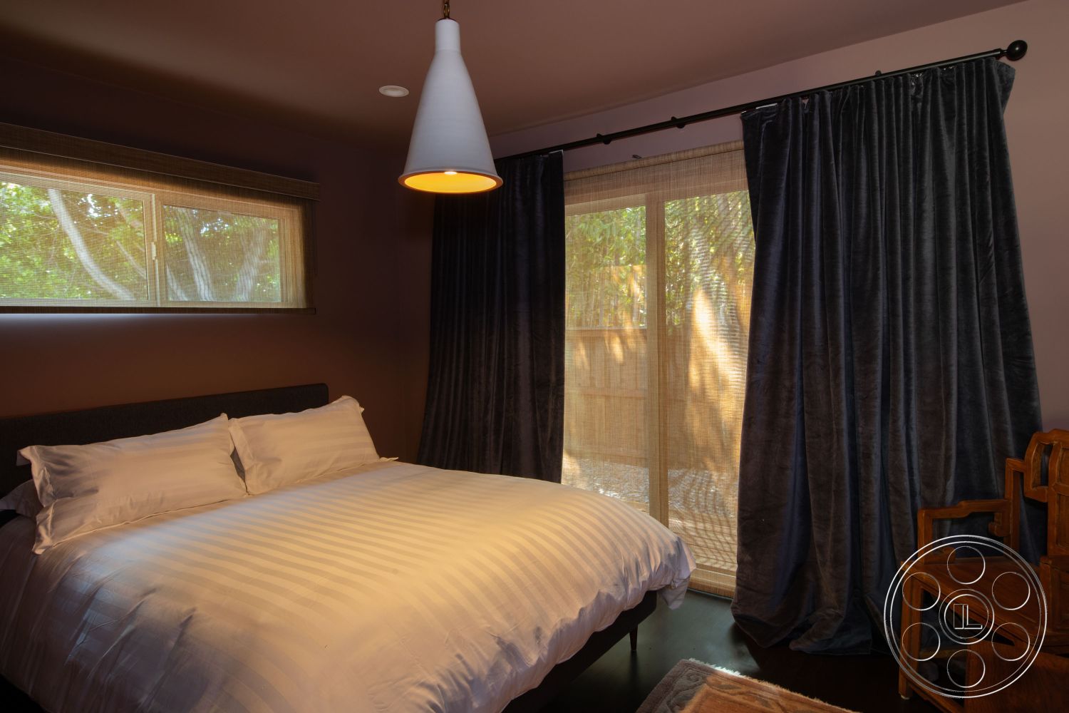 Bungalow 56 - neutral color palette, modern pendant lighting, textured plaster walls, natural light from windows, striped duvet cover, cozy bedroom atmosphere, minimalist interior design, hardwood bedroom floors, dark wood bed frame, curtains with blackout lining, exterior sliding glass door, functional wooden chair, contemporary furniture style, double-pane window, peaceful garden view