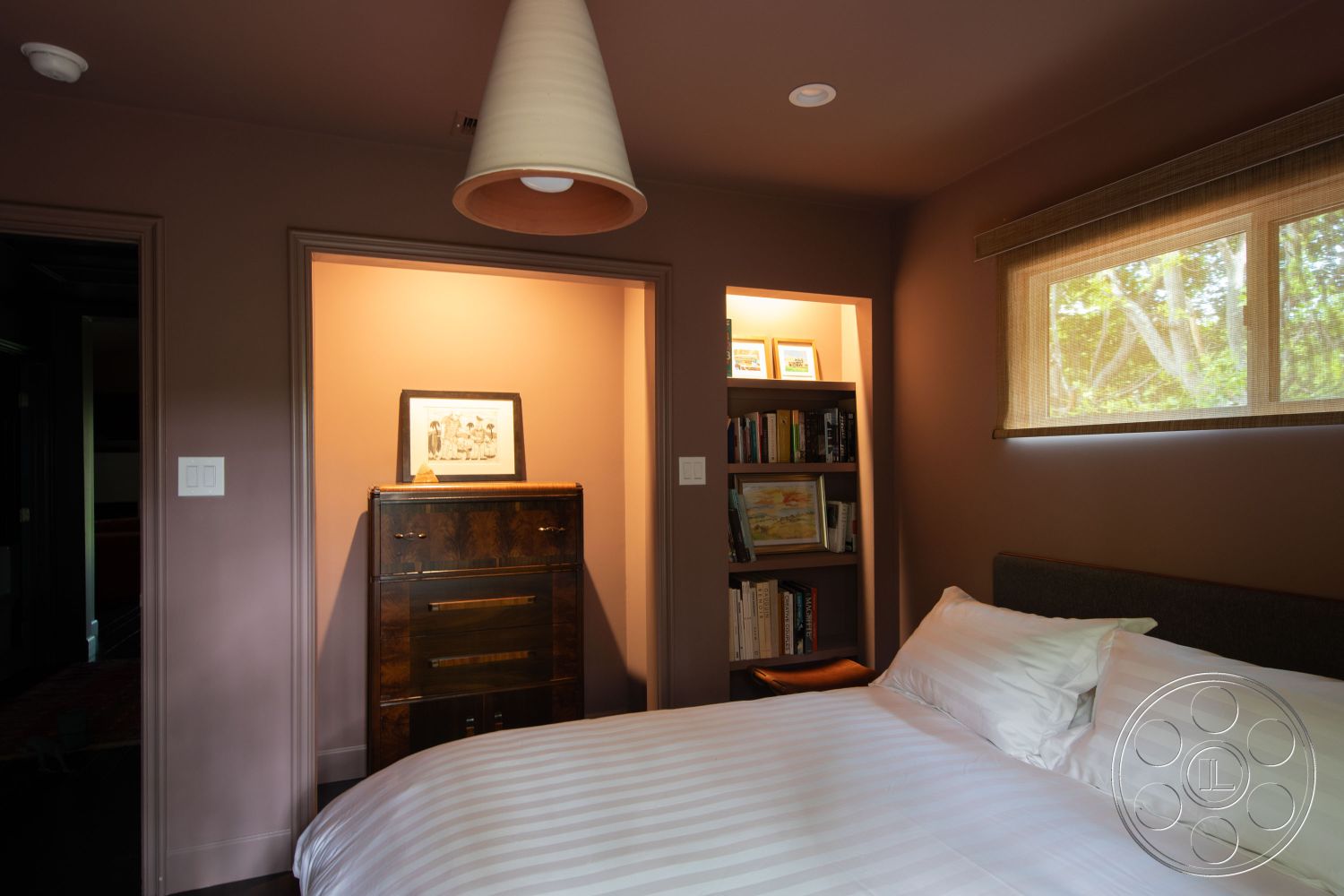 Bungalow 56 - dark hardwood flooring, contemporary lighting fixture, interior bedroom with dark brown painted walls, queen-sized bed with white striped bedding, wooden nightstand with modern design, floating bookshelves in nook area, framed artwork on display above nightstand, wood beam ceiling, natural light from window with bamboo shades, minimalist closet space, bedroom with cozy reading nook, built-in bookcase with open shelving, spacious layout with clear sight lines