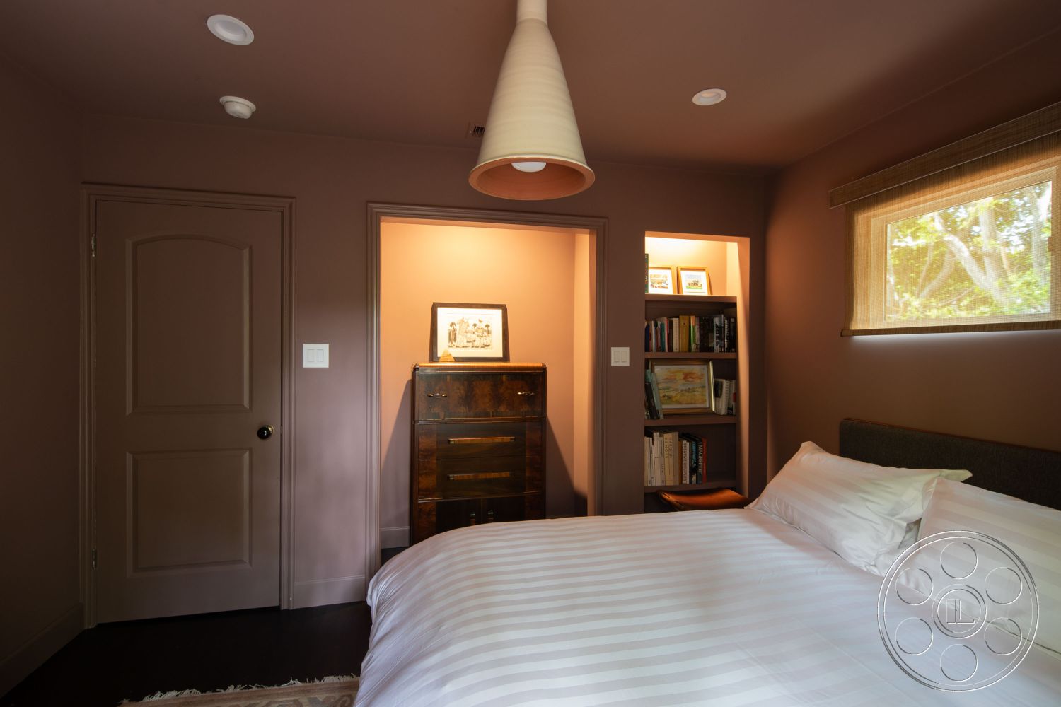 Bungalow 56 - neutral color palette, minimalist aesthetic, arched doorways, soft window treatments, striped bedding, modern pendant light fixture, dark hardwood bedroom floors, textured plaster wall finish, interior bedroom with painted walls, wooden bookshelf with books, paneled interior door, cozy atmosphere with natural light, artfully arranged wall art, built-in storage nook, contemporary bedroom design, decorative accent wall