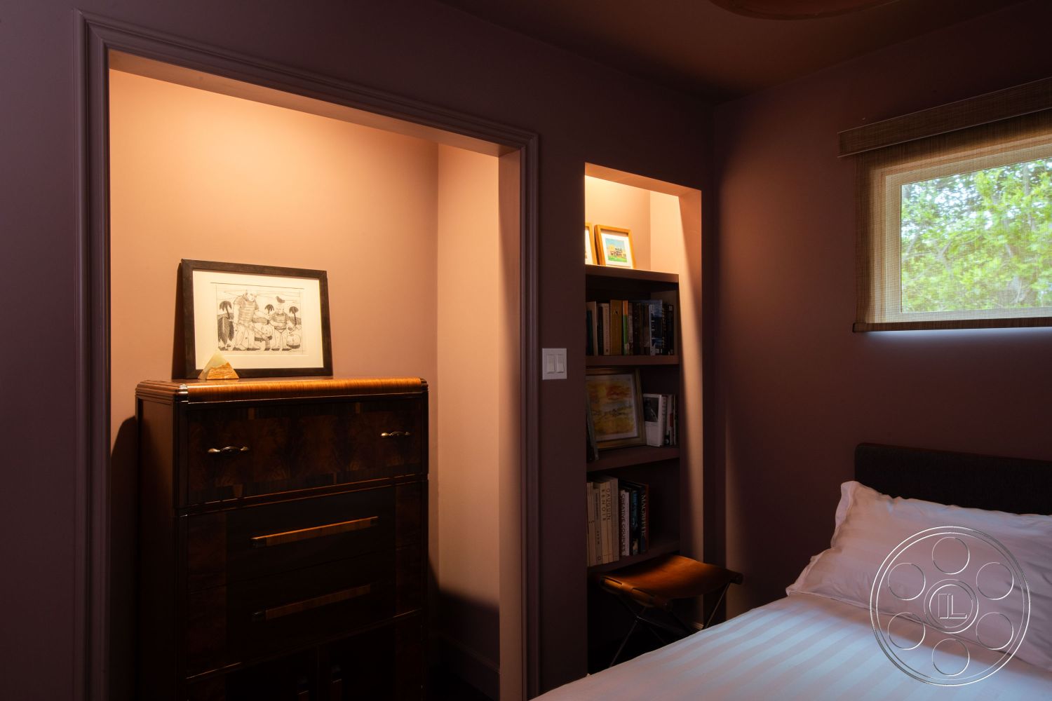 Bungalow 56 - textured wall treatments, cozy reading corner, interior bedroom space, hardwood bedroom floors, plum painted walls, modern wooden dresser, minimalist picture frame art, built-in bookshelf nook, natural light window with shade, contoured ceiling detail, neutral bedding accents