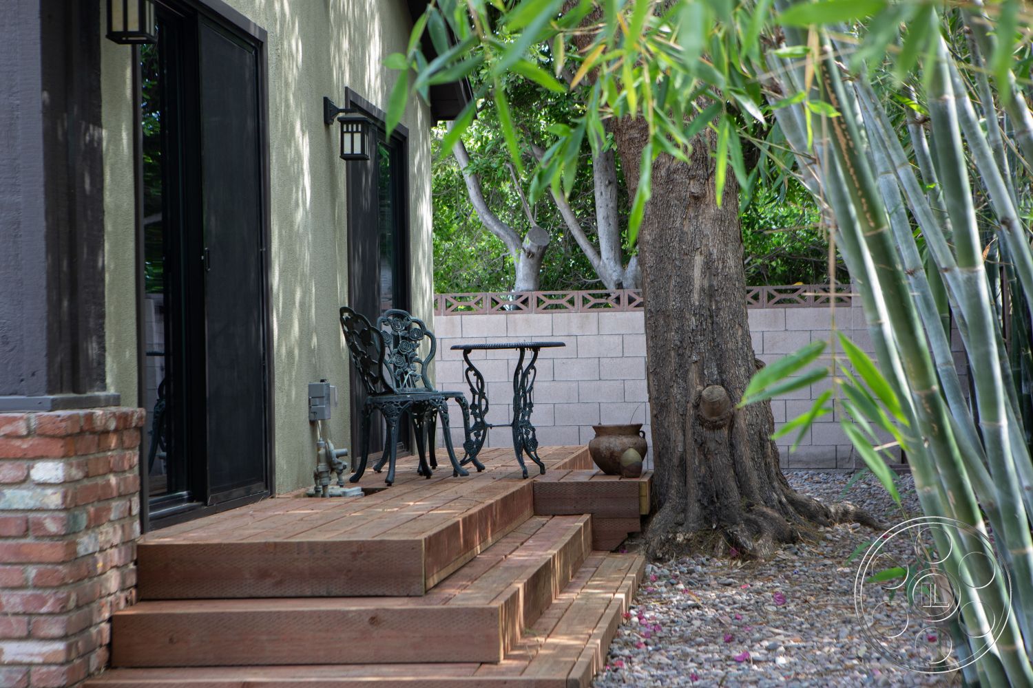 Bungalow 56 - exterior stucco walls, exterior wood deck stairs, exterior wood decking, exterior brick column, exterior metal lanterns, exterior black glass doors, exterior bamboo landscaping, exterior stone decorative planters, exterior paver patio, exterior concrete block wall, exterior shaded seating area, exterior tree shade, exterior rustic garden setting, exterior urban backyard retreat, exterior wrought iron furniture