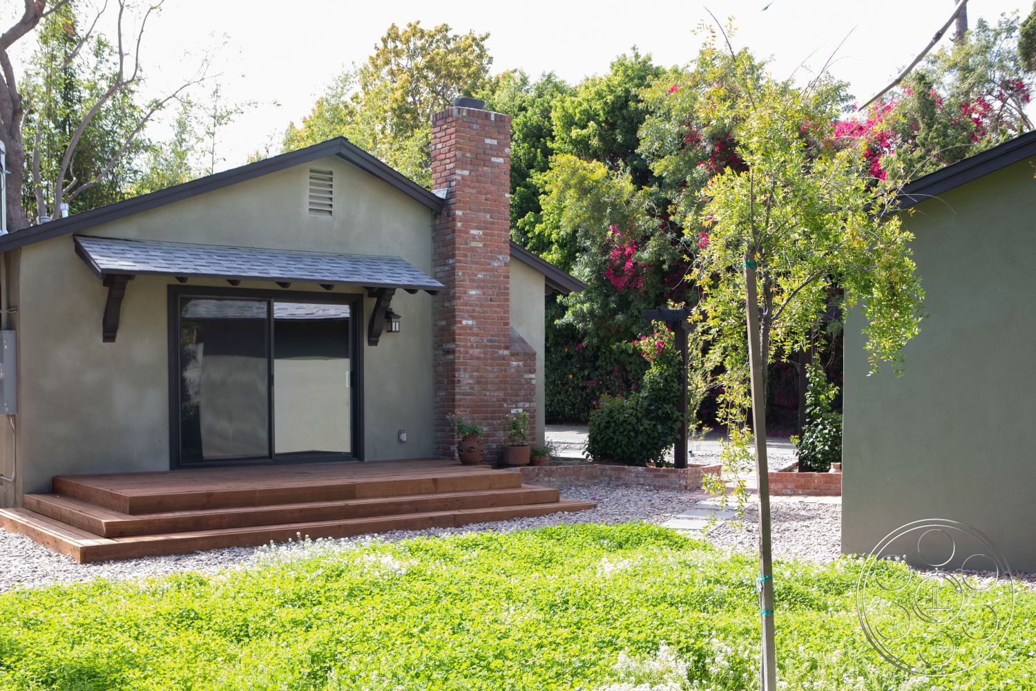 Bungalow 56 - exterior shingle roof, exterior stucco walls, exterior sliding glass doors, exterior wooden deck steps, exterior red brick chimney, exterior landscaped garden, exterior gravel ground cover, exterior green shrubbery, exterior flowering plants, exterior modern architectural style, exterior overhanging eaves, exterior wood beam supports