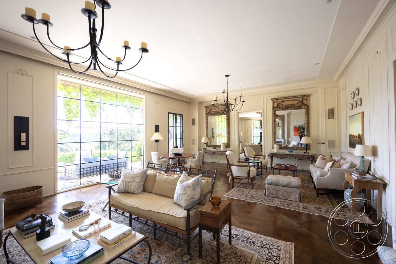 The Regent - neutral color palette, glass coffee table, textured plaster walls, large floor-to-ceiling windows, decorative wall panels, inviting and airy atmosphere, elegant area rug, hardwood living room floors, interior living room, exposed wood trim details, traditional chandelier lighting, high ceiling with decorative molding, varied seating arrangement with upholstered chairs, retro wall mirrors, sunlit interior with natural light, french door to exterior patio, framed landscape artwork, elegant home decor accessories, spacious layout with open flow