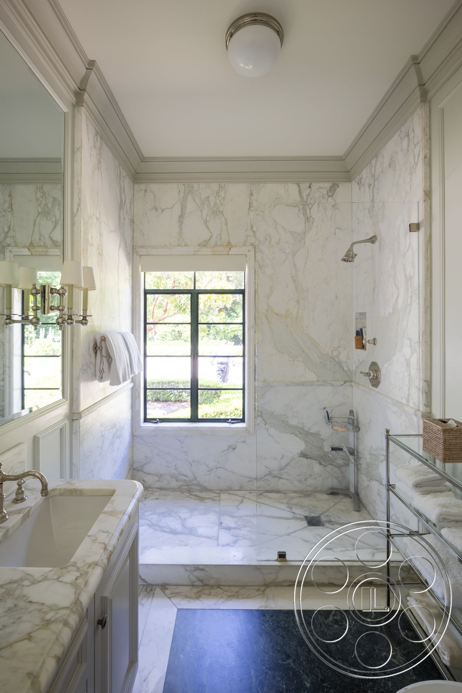 The Regent - glass shower enclosure, spa-like ambiance, luxurious interior, modern bathroom design, marble bathroom walls, marble shower flooring, marble shower step, white vanity with chrome faucet, black stone bathroom flooring, framed mirror with wall sconces, black framed window with garden view, molding details on ceiling, open space shower area, natural light flooded bathroom