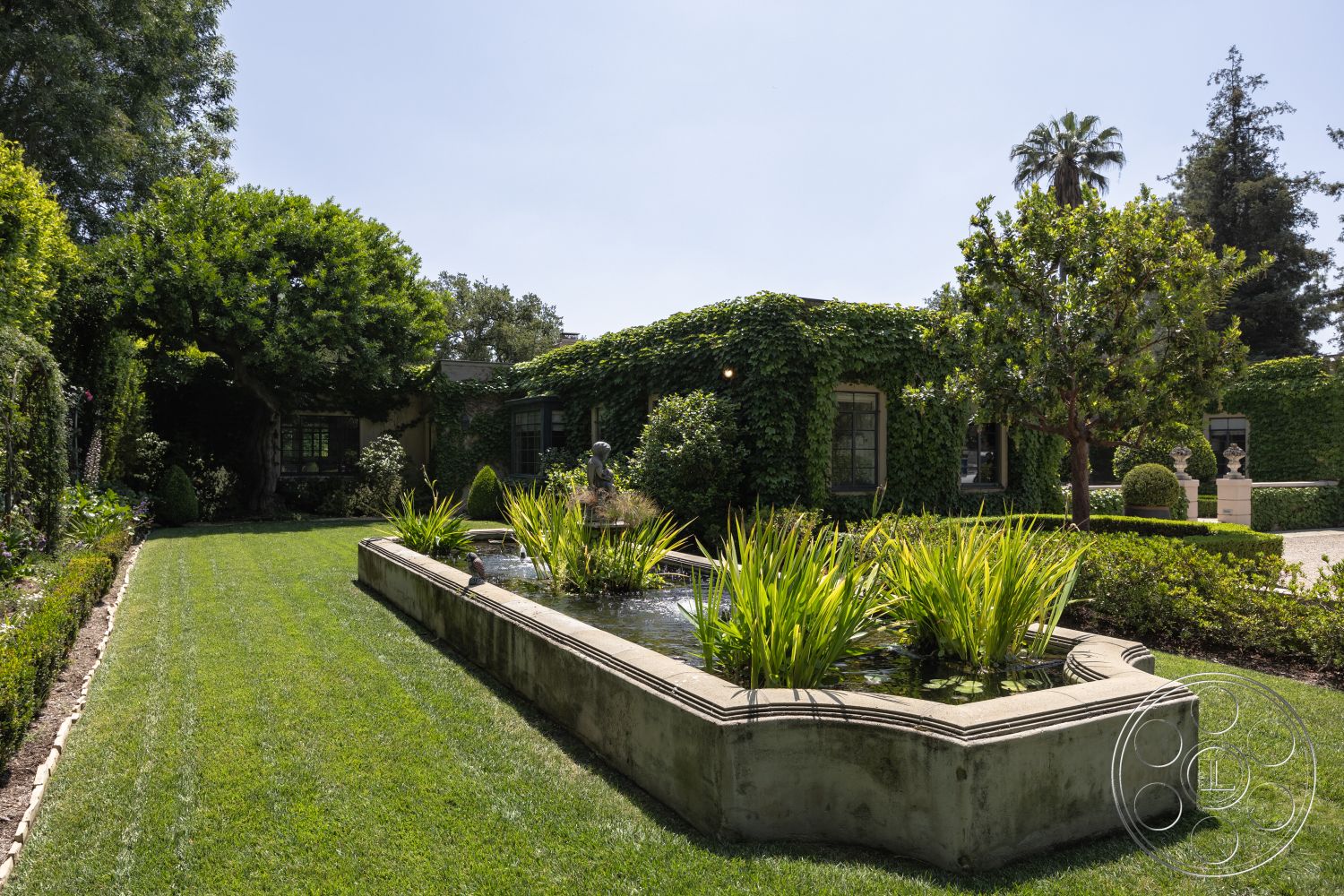 The Regent - green grass lawn, large palm trees, sunny outdoor space, modern residential architecture, brick pathways, private garden oasis, courtyard home design, rectangular pond shape, exterior garden setting, concrete pond border, lush plant landscaping, vines covering building facade, boxwood hedge borders, ornamental stone statues, decorative water features, environmentally integrated landscaping