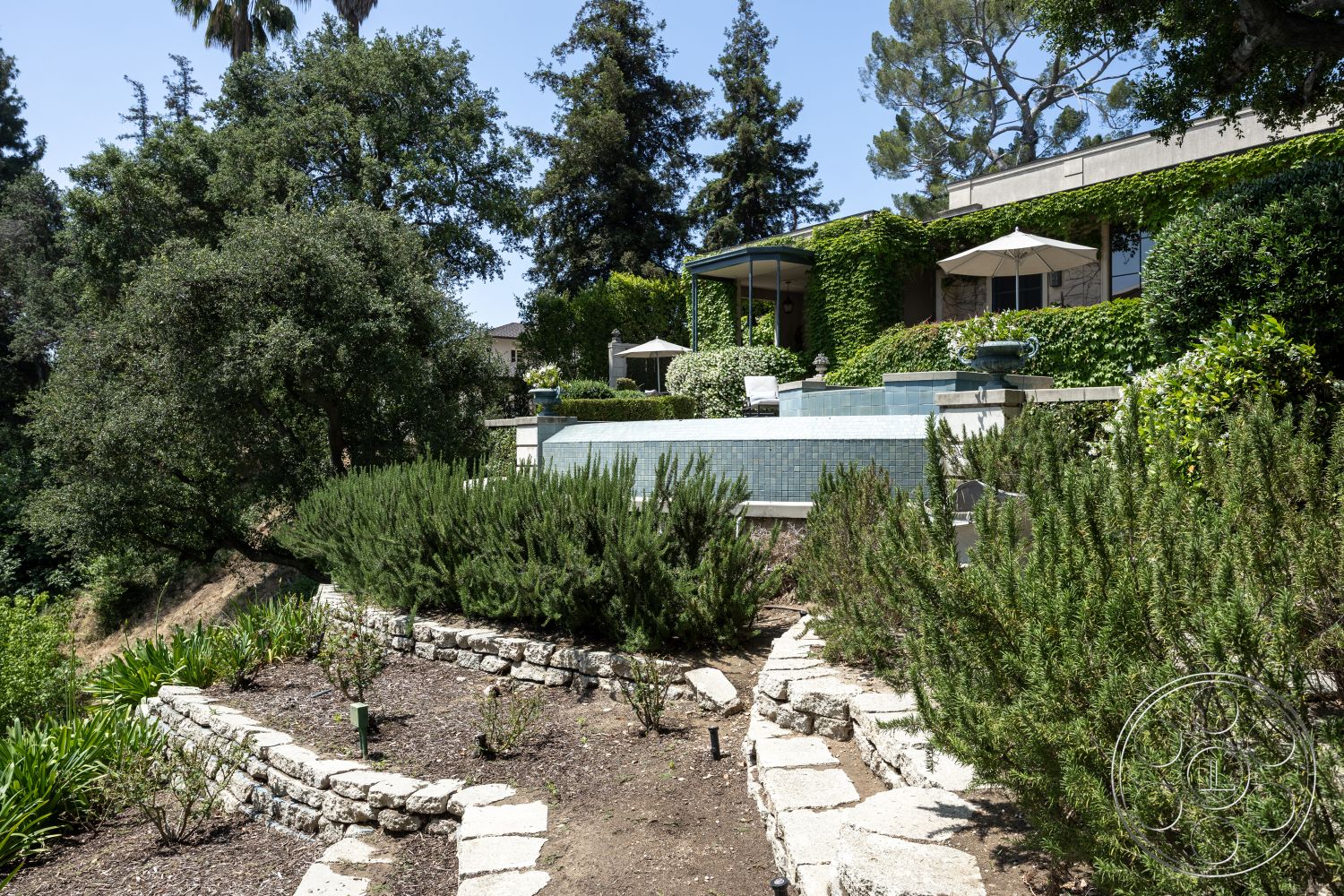 The Regent - fenced garden area, mature trees, outdoor entertaining space, natural stone pathway, rectangular pool, wooden patio furniture, tiled pool deck, stone retaining wall, terraced garden, lush green landscaping, exposed aggregate concrete patio, contemporary home design, exterior garden setting, tropical plant accents, paver stone walkways, parasol shading, irrigation system, sun-drenched exterior, aggregate concrete steps