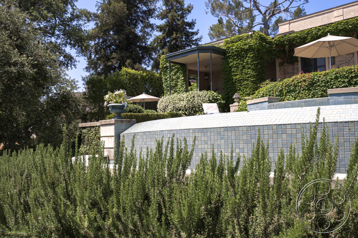 The Regent - exterior, lush greenery, modern outdoor furniture, concrete patio, arched entryway, cobblestone path, decorative urns, Mediterranean architectural style, poolside lounge area, terraced landscaping, shade umbrellas, perennial flower beds, city skyline backdrop, ceramic tile pool wall, stone garden wall, vegetable garden, vine-covered trellis, stucco home facade, exposed brick planters