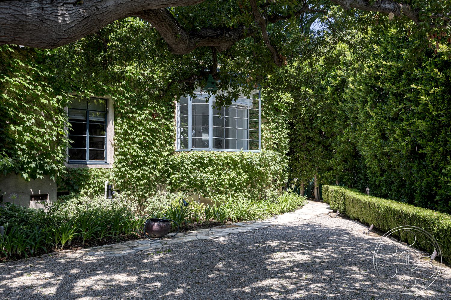 The Regent - exterior, landscaped garden, natural stone accents, stone pathway, organic shapes, stucco walls, gravel driveway, privacy hedges, outdoor light fixtures, softscape, urban garden setting, low-maintenance shrubs, grid-style windows, beveled glass window trim, lush green ivy, curved garden edges, shaded walkways