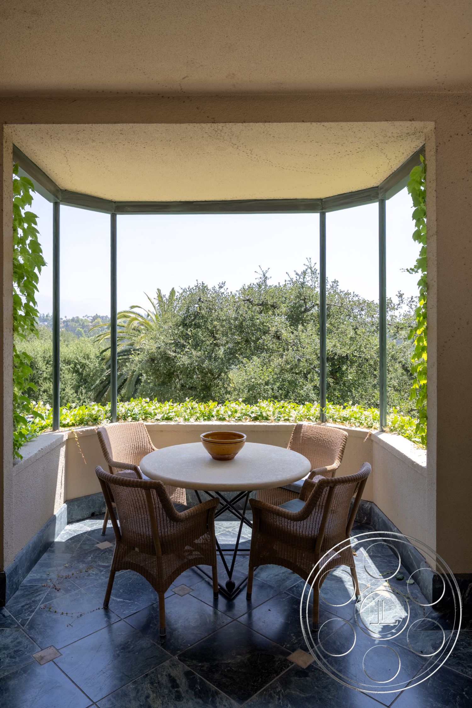 The Regent - natural light, open space, contemporary decor, modern design, large glass windows, greenery view, textured plaster walls, wicker dining chairs, interior sunroom, slate floor tiles, round concrete table, outdoor eating area