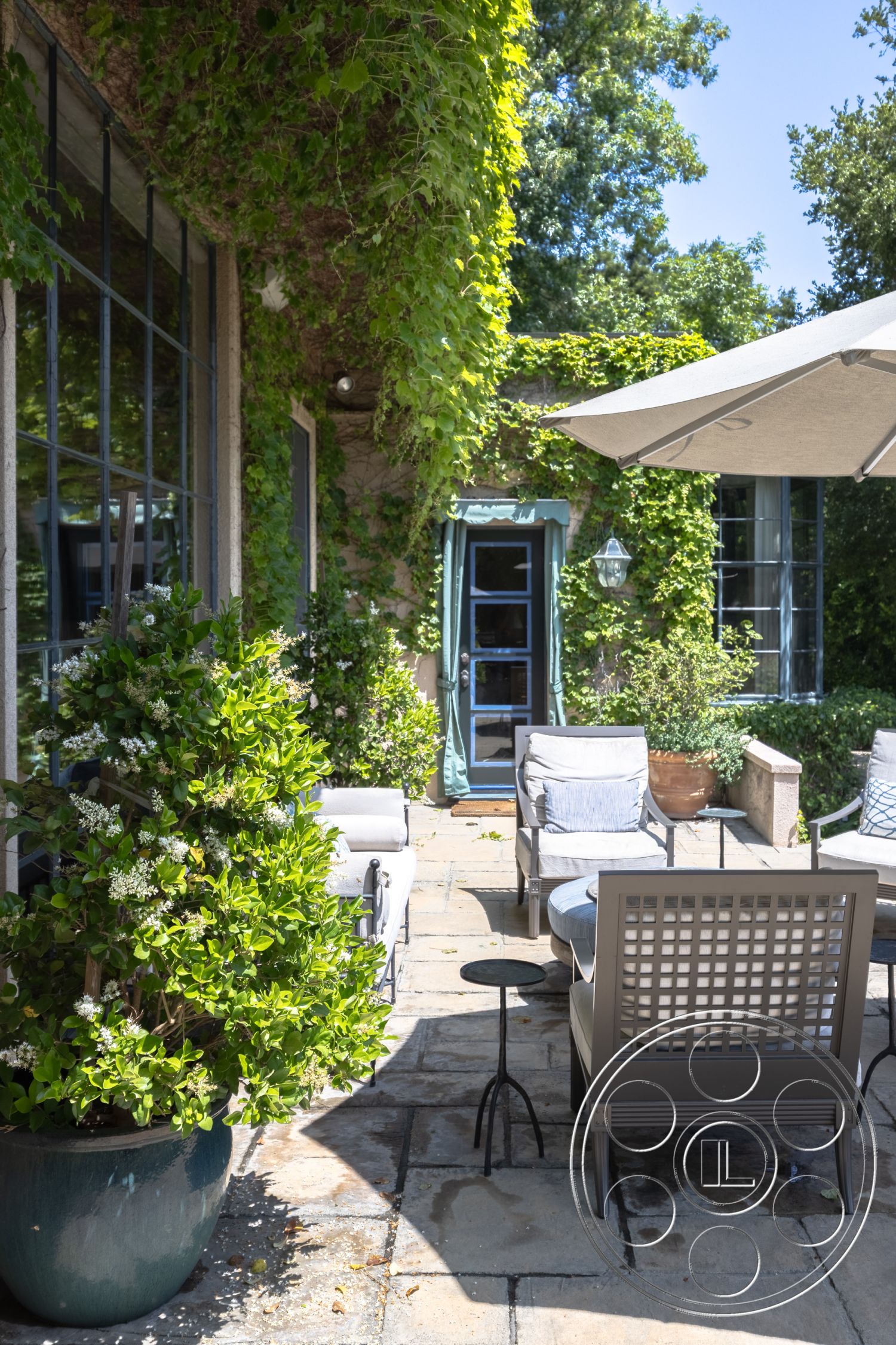 The Regent - natural light, exterior, garden view, smooth concrete surface, woven outdoor furniture, casual lounging space, slate stone pavers, stone patio flooring, blue glass door, greenery and climbing vines, potted shrubs, umbrellas for shade, custom landscape design, rustic outdoor seating area, outdoor table with metal accents