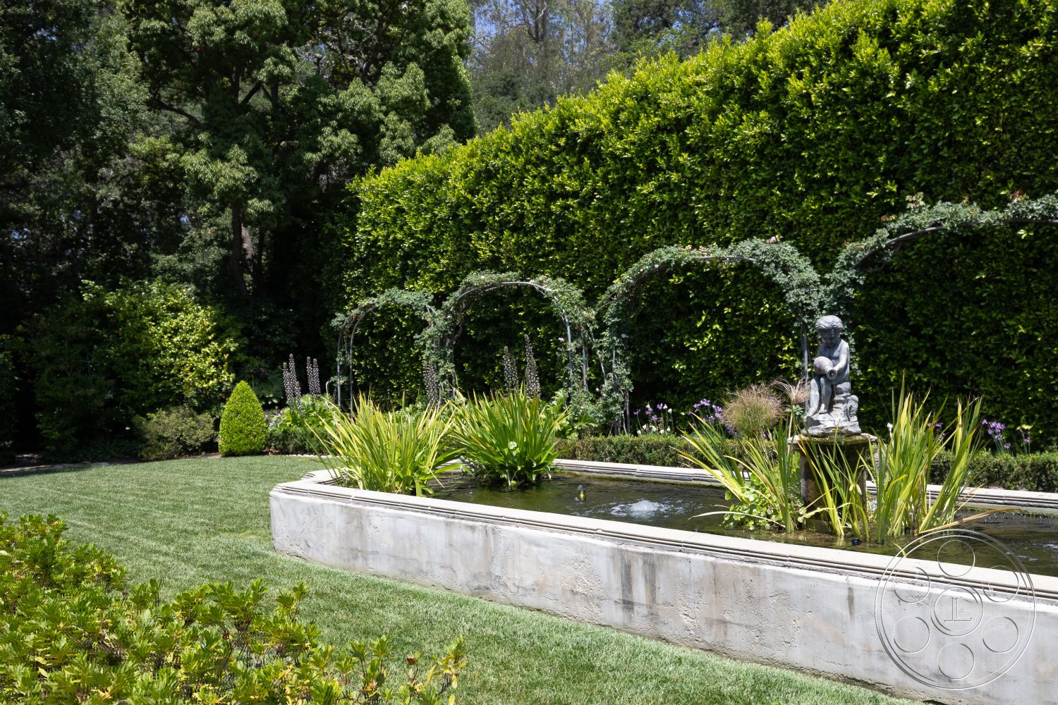 The Regent - manicured lawn, natural stone pathway, garden seating area, sunny outdoor space, hedge privacy wall, lush green landscaping, circular garden layout, botanical garden setting, exterior concrete garden fountain, rectangular concrete planter, wooden garden trellis with climbing plants, sculptural stone statue, ornamental grasses in garden, flower beds with colorful blooms, water feature with gentle flow