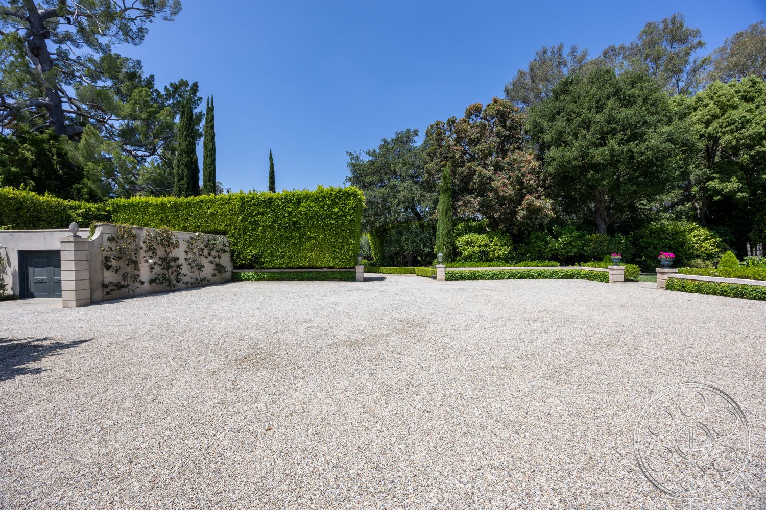 The Regent - tall cypress trees, sunny outdoor area, gravel driveway, hedge privacy screen, planted flower beds, drought-resistant landscaping, landscaped garden setting, curved garden pathways, exterior column features, ornamental stone pillars, modern fence design, outdoor leisure space, natural stone wall accents, exterior building facade, open outdoor layout