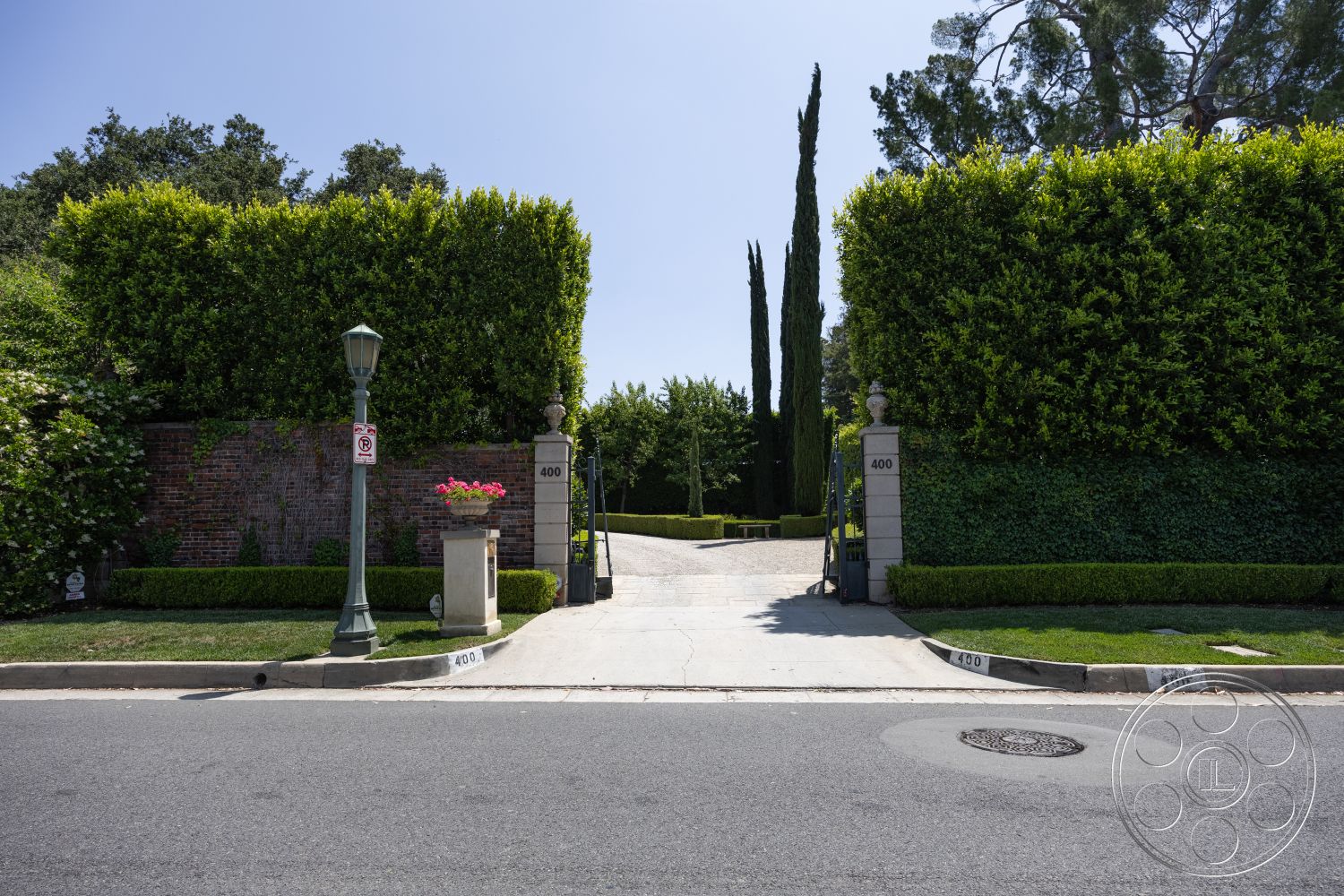 The Regent - suburban setting, circular driveway, concrete driveway, manicured lawn, landscaped garden area, exterior brick wall, interior hedges, cast iron lamppost, stone gate pillars, mature cypress trees, flower planter, private gated entrance