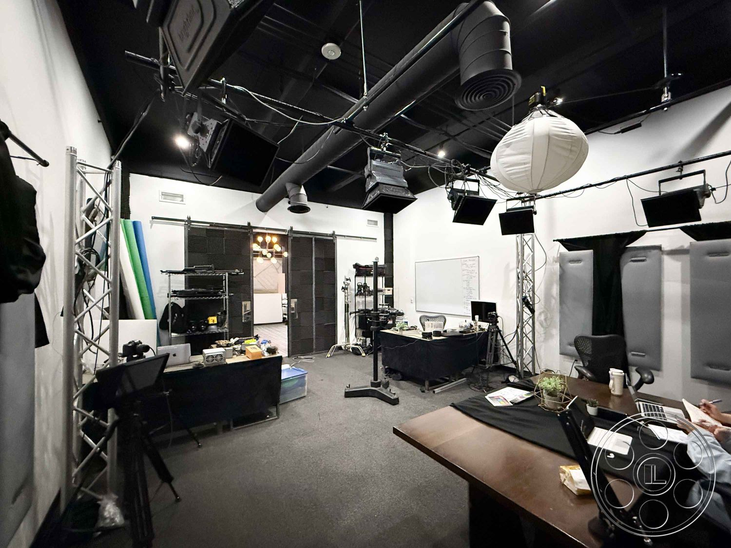 Office 124 - creative workspace, metal shelving units, black office chairs, glass partition doors, dark carpet flooring, wooden conference table, interior studio space, black acoustic wall panels, exposed ceiling with ductwork, LED studio lighting fixtures, whiteboard wall, studio equipment in background, electric green and blue backdrop, modern industrial style, functional work area