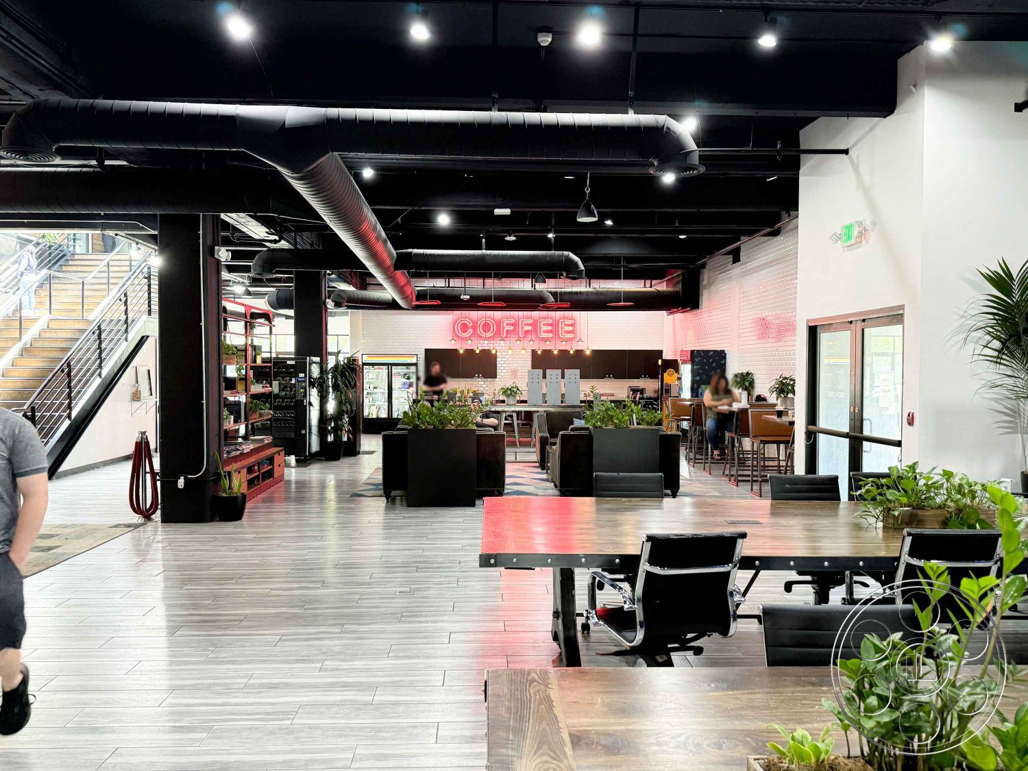 Office 124 - tile flooring, urban setting, black metal chairs, large floor-to-ceiling windows, open layout design, contemporary bar area, exposed ductwork ceiling, interior coffee shop, dark wood communal tables, bright neon signage, greenery indoor plants, steel railing staircase, modern shelving units, industrial style decor, polished concrete accent wall