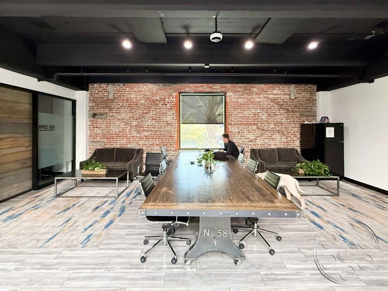 Office 124 - exposed brick accent wall interior, wood panel accent wall interior, dark wood beam ceiling interior, large rectangular conference table interior, industrial steel table base interior, modern office chairs interior, tile flooring with blue accents interior, large windows with natural light interior, green plants decor interior, minimalistic office layout interior, open concept workspace interior, brick feature wall interior, contemporary office style interior, comfortable seating area interior, modern refrigerator interior
