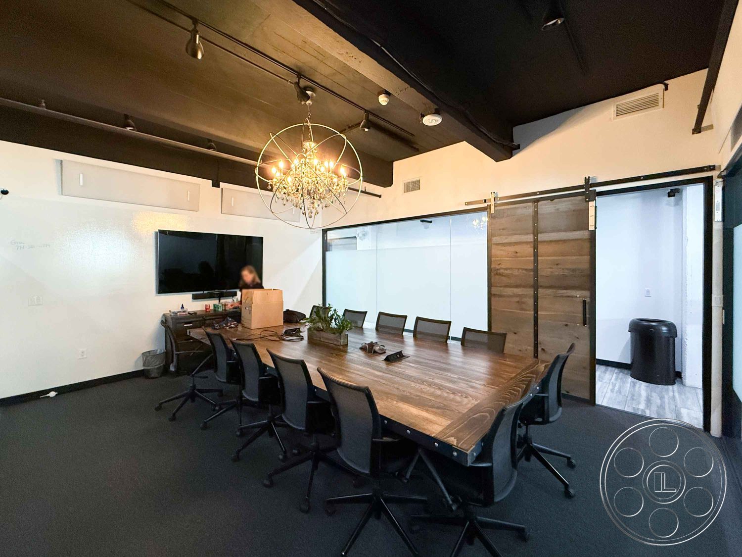 Office 124 - minimalist design, wall-mounted television, black office chairs, sliding barn door, white painted walls, open layout design, modern chandelier lighting, urban office setting, glass partition wall, interior conference room, dark carpet flooring, wood table with metal accents, black ceiling with exposed beams, admin workspace with plants