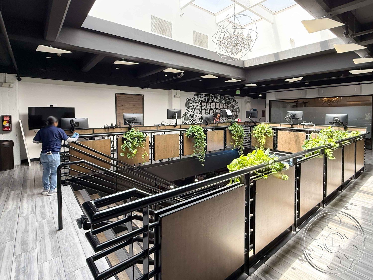 Office 124 - contemporary aesthetic, exposed wood ceiling beams, glass partition walls, modern office environment, industrial-style lighting fixtures, dark wood paneling accents, floating black metal stair railings, rectangular open office layout, wooden desk surfaces, textured plaster wall with graphic design, high ceilings with skylights, tile flooring with wood-like appearance, greenery on office walls, multi-level workspace, creative collaborative space, urban industrial design