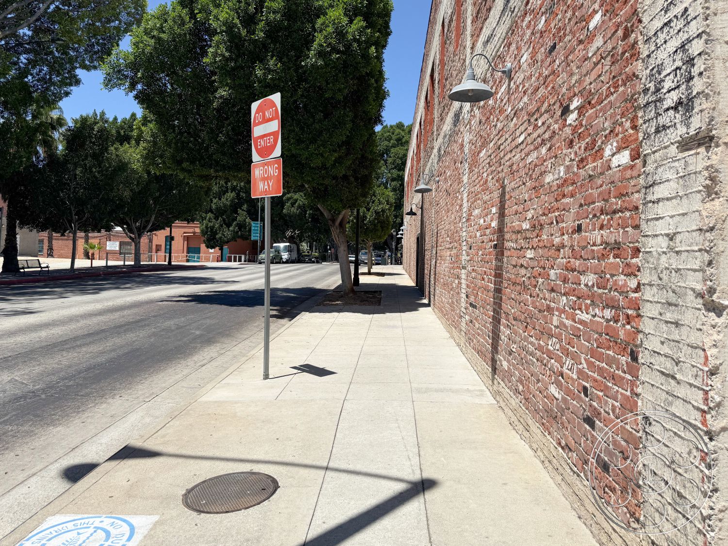 Office 124 - urban setting, tree-lined street, landscape trees, metal wall sconces, commercial building exterior, exposed brick wall exterior, concrete sidewalk pavement, flat concrete pavement, red brick masonry, street sign post, textured brick surface, adjacent roadway, public sidewalk, light fixture detail, city environment, civic infrastructure