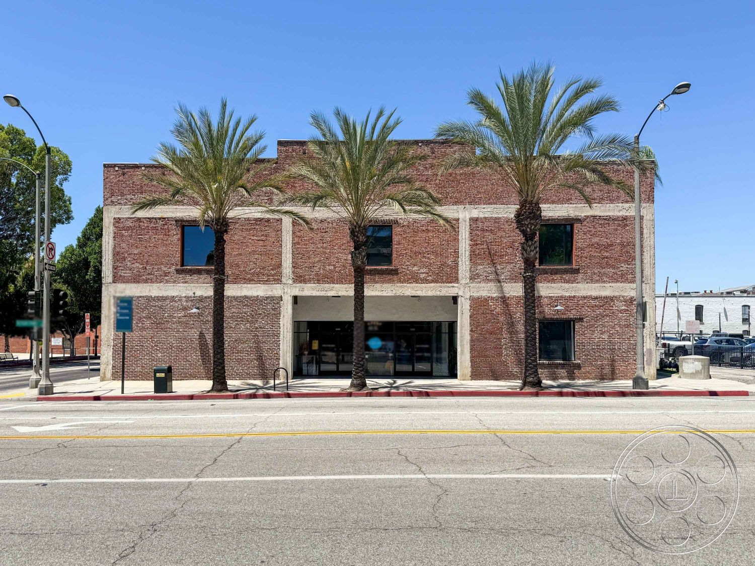 Office 124 - urban setting, concrete sidewalk, flat roof design, palm trees landscaping, two-story commercial building, exterior brick walls, exposed concrete structure, modern storefront entrance, large fixed windows, steel and glass facade details