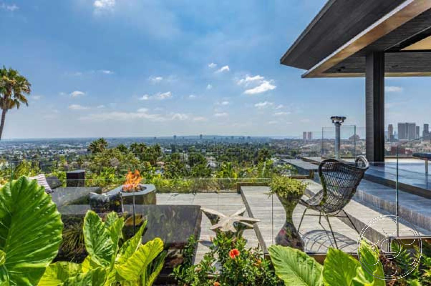 Modern 507 - city skyline view, exterior stone patio flooring, contemporary outdoor living space, floor-to-ceiling glass windows, exterior glass railing, palm tree landscaping, exterior fire pit seating area, exterior lounge chair, landscaped garden with tropical plants, modern infinity pool edge, rectangular outdoor deck, exposed steel structural beams, slate tile outdoor flooring, open-air entertainment area, sunny hillside location