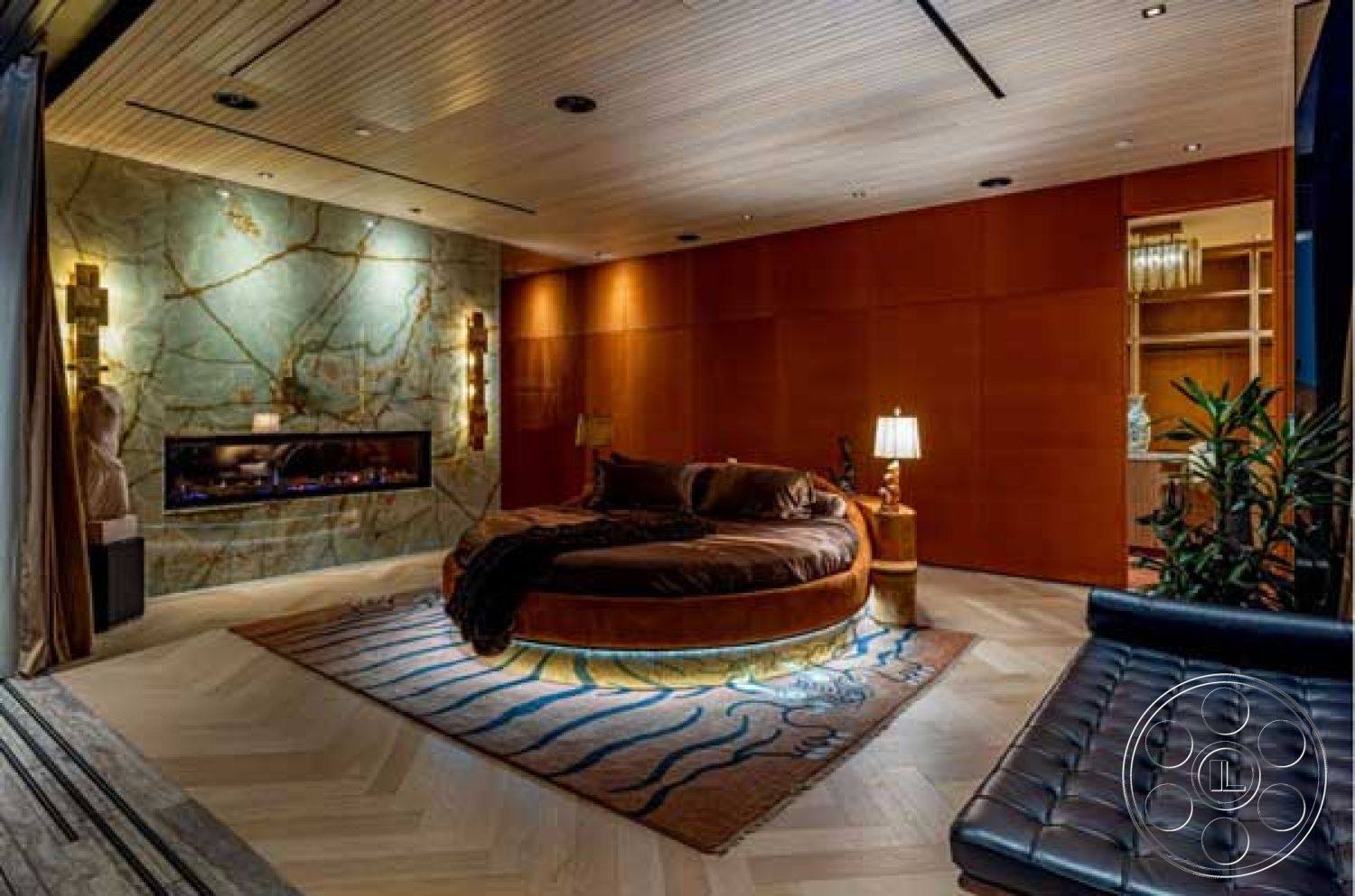 Modern 507 - contemporary bedside lamp, recessed ceiling lights, wood panel accent wall, exposed stone feature wall, herringbone hardwood flooring, round platform bed, modern fireplace with a custom mantle, luxurious area rug with artistic design, tall plants for interior decor, open shelving unit, cozy seating area with leather sofa, elegant warm color palette, architectural wood ceiling with linear design