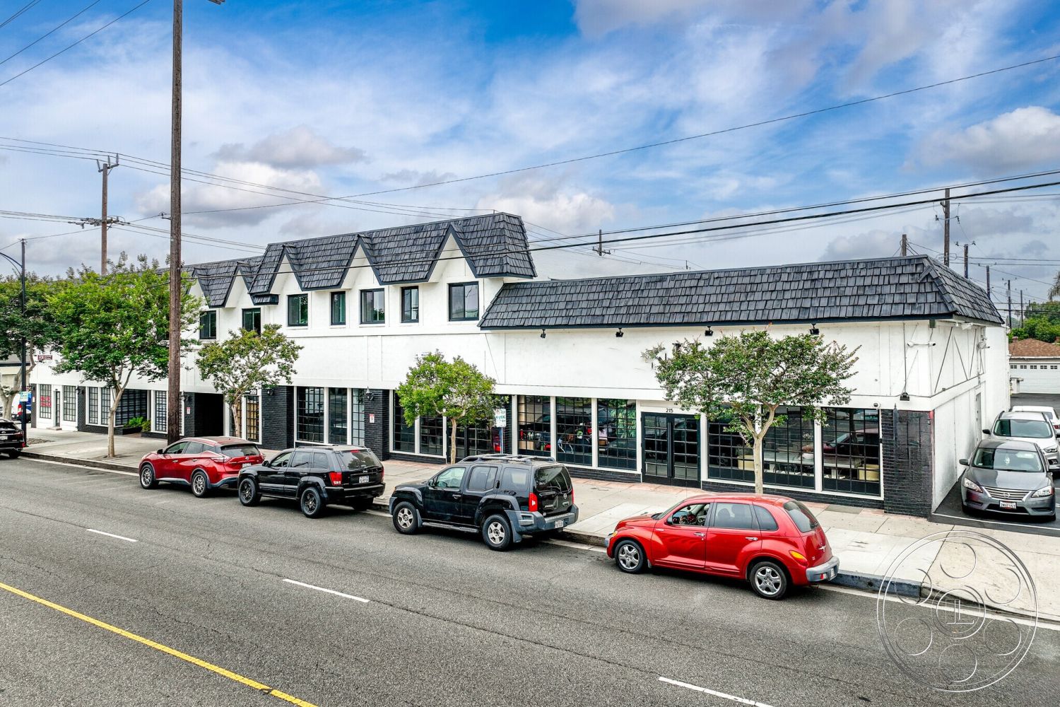 Office 125 - neutral color palette, exterior, asphalt shingle roof, masonry accents, overhead power lines, gabled roof shape, stucco building facade, large glass storefront windows, black painted brick base, sidewalk parking area, landscaped trees in front, urban street view, two-story building design, modern commercial architecture, multiple pedestrian entrances, traffic-friendly setting, flat facade, symmetrical building layout