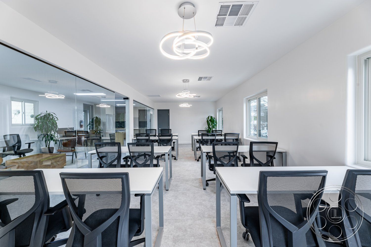 Office 125 - minimalist decor, neutral color palette, natural light from large windows, glass partition walls, potted indoor plants, light grey carpet flooring, interior office space, open workspace layout, light-colored drywall walls, modern design furniture, white rectangular office desks, mesh ergonomic office chairs, in recessed ceiling lighting, suspended circular light fixtures, firm meeting area