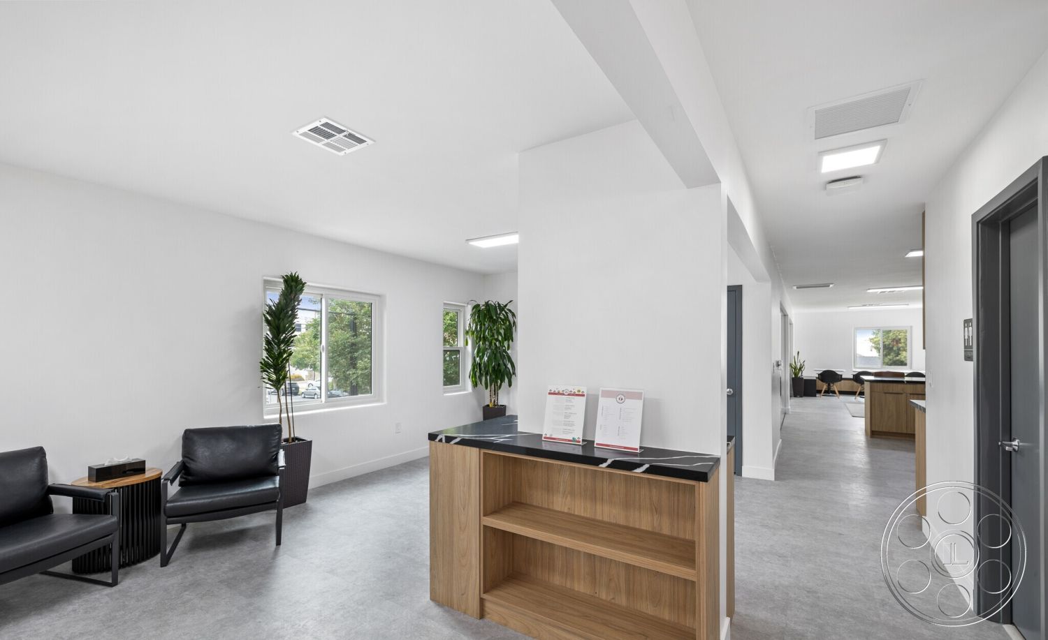Office 125 - neutral color palette, large windows, contemporary design, clean lines, open floor plan, wooden cabinetry, concrete flooring, interior space, black countertop, minimalist furniture, functional workspace, planter with greenery, bright ambient lighting, efficient layout, white painted walls, modern reception desk, welcoming reception area, horizontal wood slat accent, black leather lounge chairs, accessible hallways