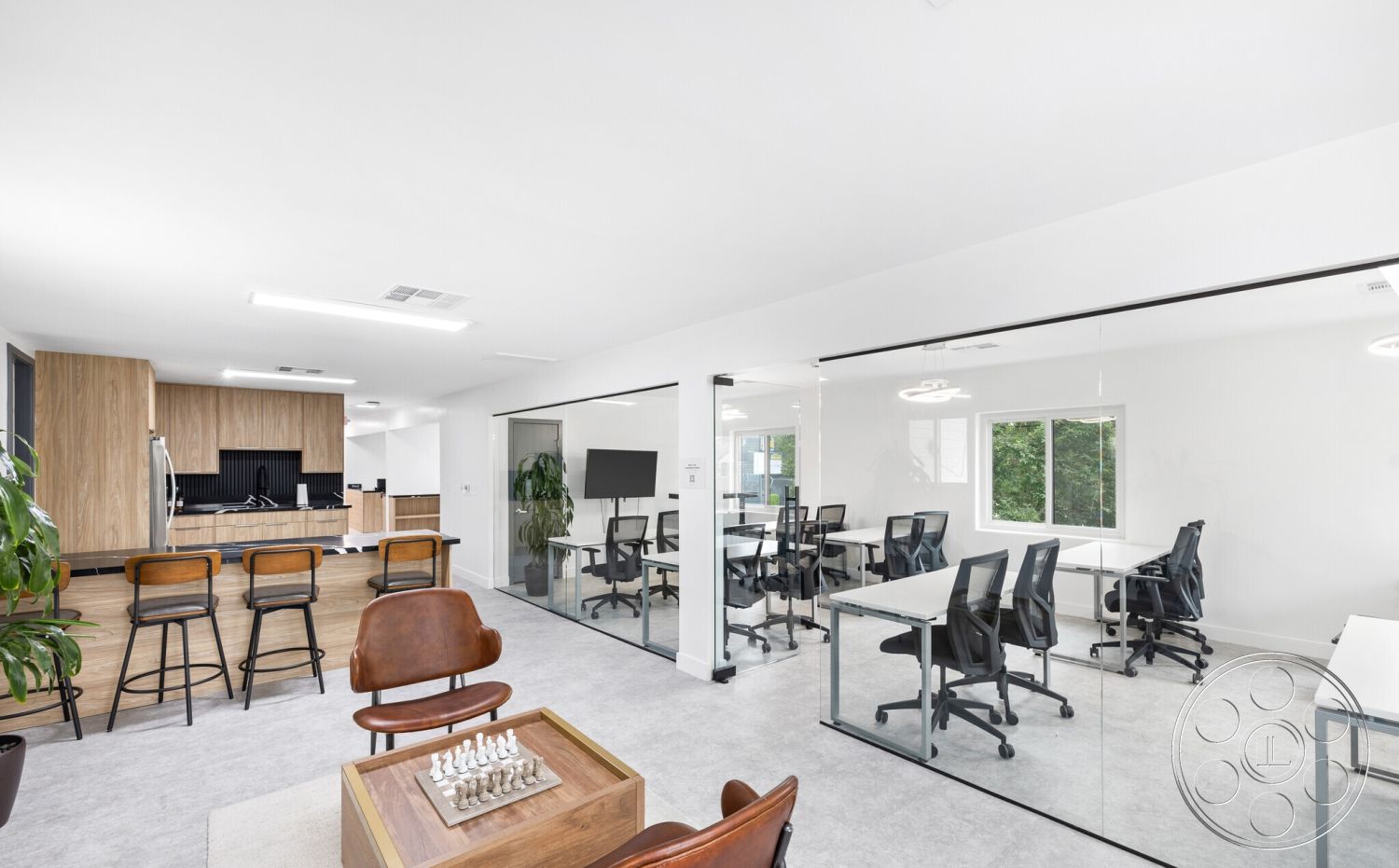 Office 125 - neutral color palette, minimalist design, open floor plan, stainless steel appliances, wood accent wall, natural light from windows, glass partition walls, interior office space, wood kitchen cabinetry, island bench with bar stools, light gray carpet flooring, modern office chairs, contemporary recessed lighting, chess table in common area, desktop workstations, green indoor plant decoration, small meeting room, spacious work environment, multifunctional workspace