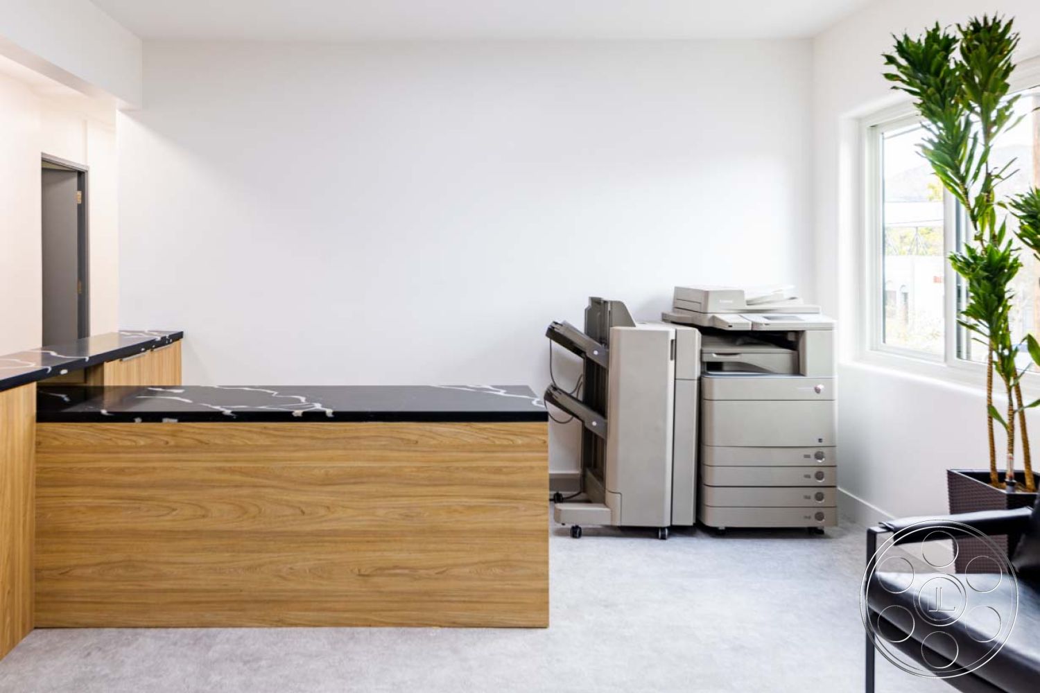 Office 125 - neutral color palette, natural lighting, open layout, floor-to-ceiling windows, minimalistic design, green indoor plant, white painted walls, modern office space, contemporary office furniture, functional workspace design, walnut reception desk with black marble countertop, luxury vinyl plank flooring, exposed wood grain details, tech-enabled workspace, copier machine area