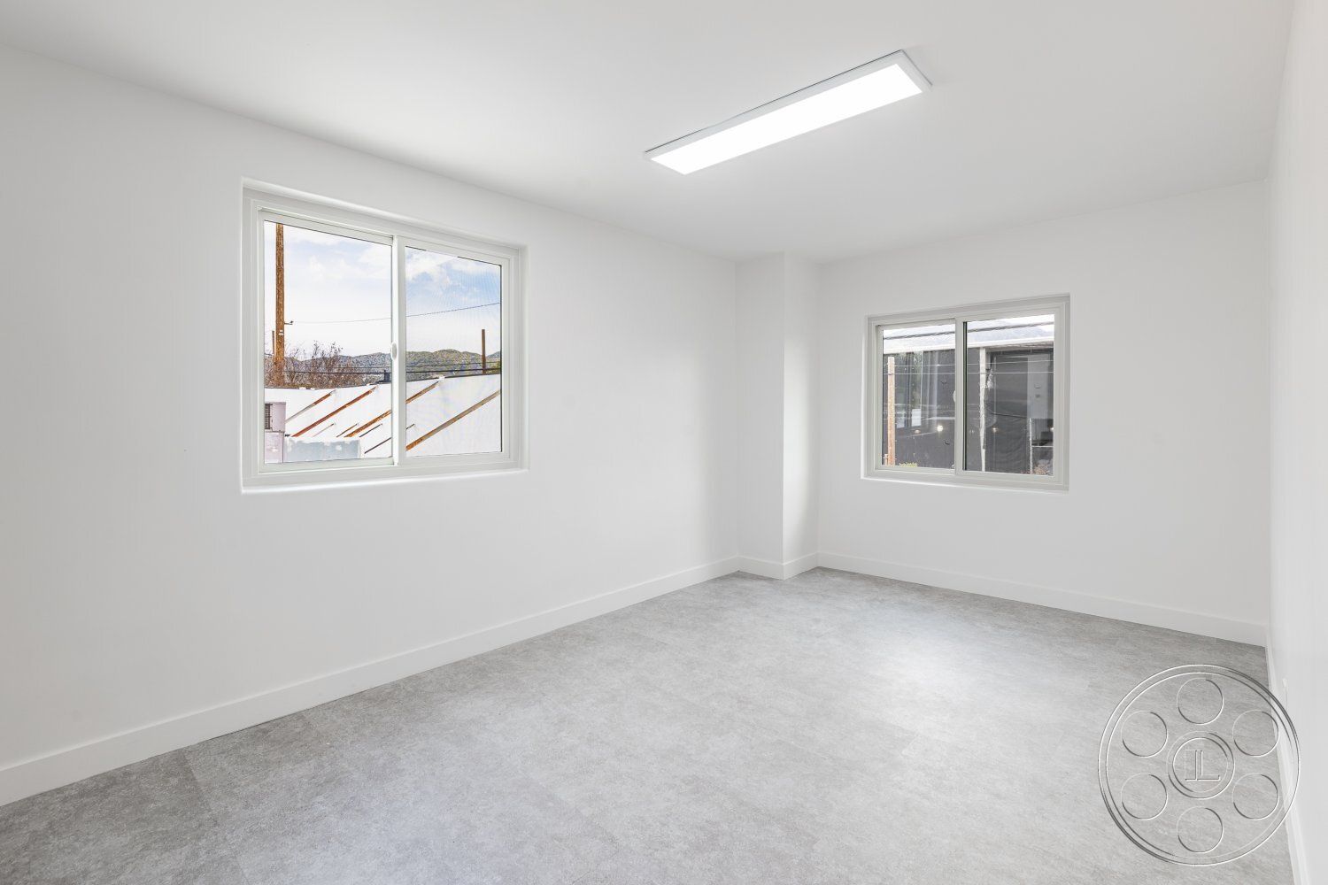 Office 125 - neutral color palette, natural light, contemporary style, minimalist design, open layout, interior space, urban setting, sparse furnishings, corner windows, white painted walls, gray vinyl flooring, single-pane windows, modern linear ceiling light