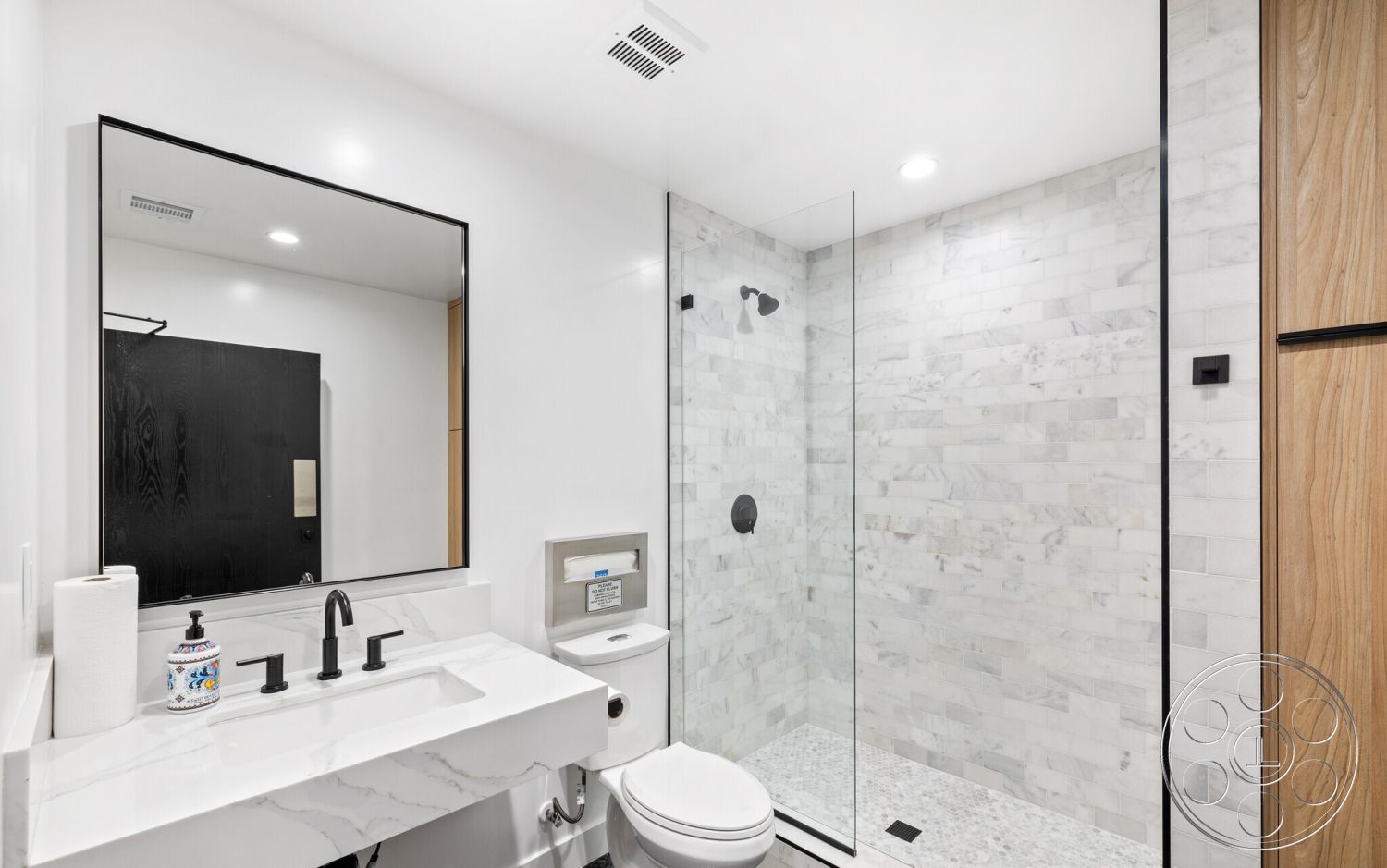 Office 125 - bathroom, textured wall tiles, recessed lighting, minimalist design elements, light wood cabinetry, large format tiles, interior bathroom, glass shower doors, marble shower walls, contemporary bathroom sink, black faucets, white bathroom vanity, mirror with black frame, monochrome color scheme, built-in toilet, stone shower floor