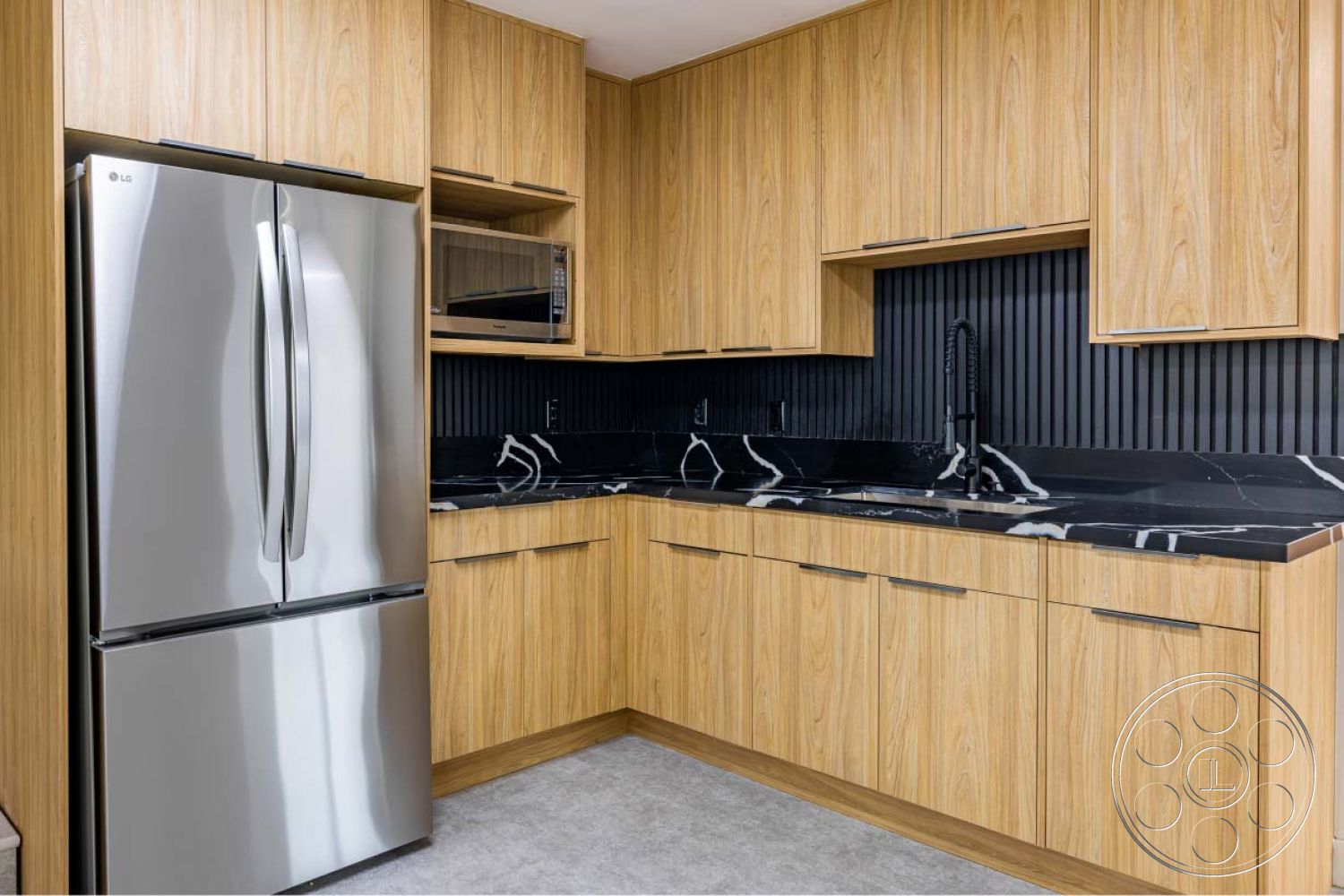 Office 125 - stainless steel refrigerator, interior kitchen, wood veneer cabinetry, black marble countertop with white veining, black textured backsplash, modern faucet with a pull-down sprayer, open shelving for kitchen storage, grey vinyl flooring, horizontal wood panel accent wall, integrated microwave, brushed nickel cabinet handles, slim profile design cabinetry