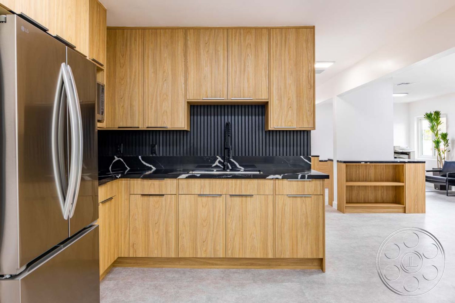Office 125 - concrete flooring, stainless steel refrigerator, modern minimalist architecture, interior kitchen cabinets made of wood veneer, black quartz countertop with white veining, slat wall paneling behind the kitchen sink, open concept kitchen layout, horizontal wood grain pattern on cabinetry, high-efficiency kitchen appliances, bright open kitchen space with natural light