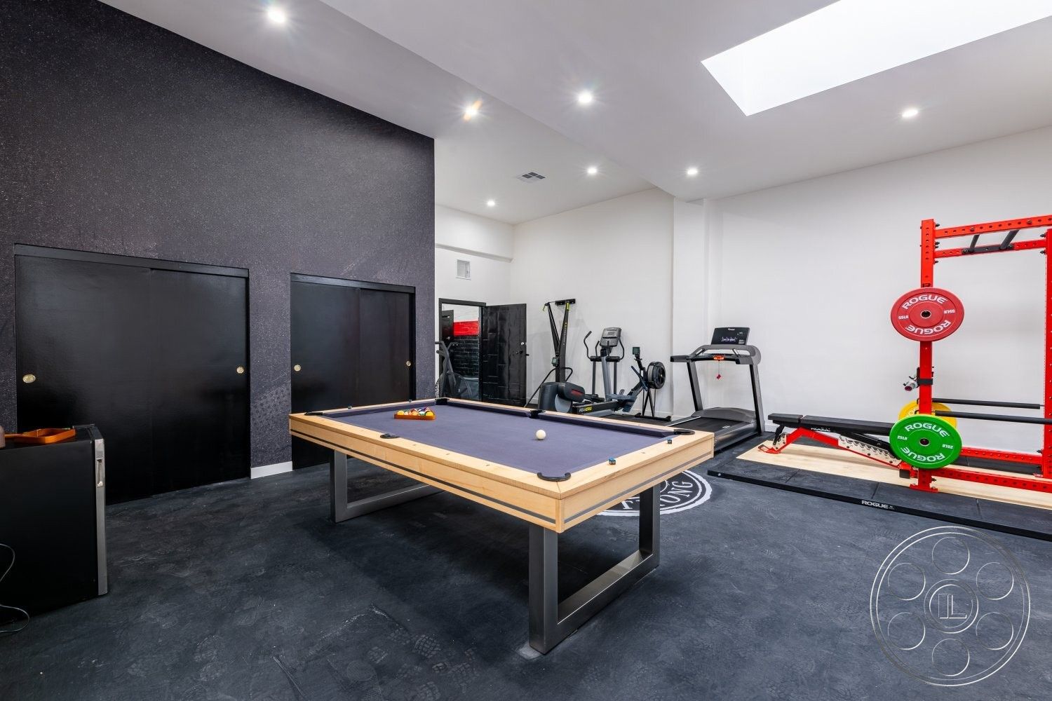 Office 125 - pool table, minimalist design elements, smooth concrete flooring, multi-functional space, skylight ceiling, bright recessed lighting, exposed black wall treatment, wood billiard table with steel frame, black closet doors, modern fitness equipment, home gym space, interior recreation room